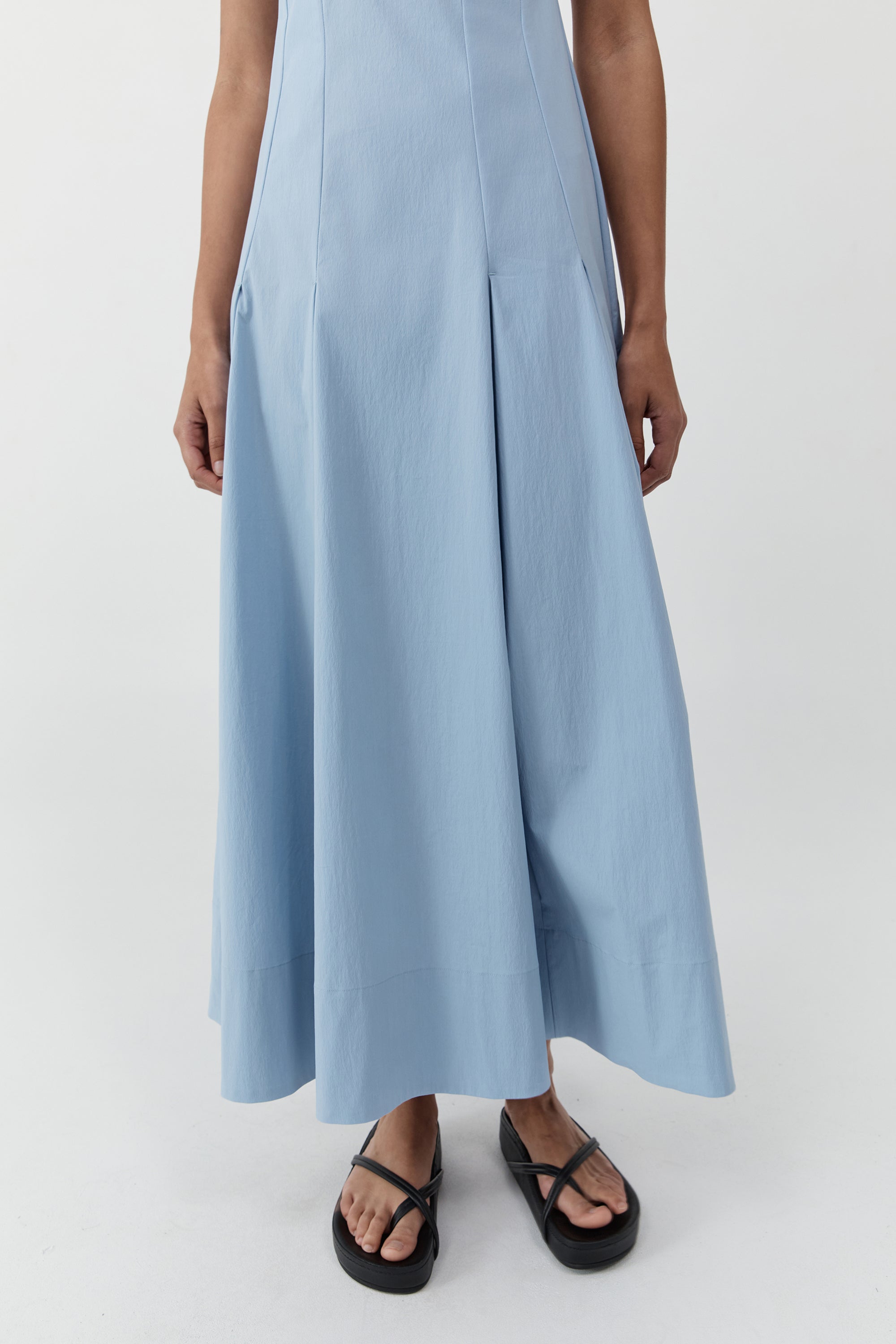 Lower half of a woman wearing the st. agni everyday cotton pleated dress in sky in front of a cream background