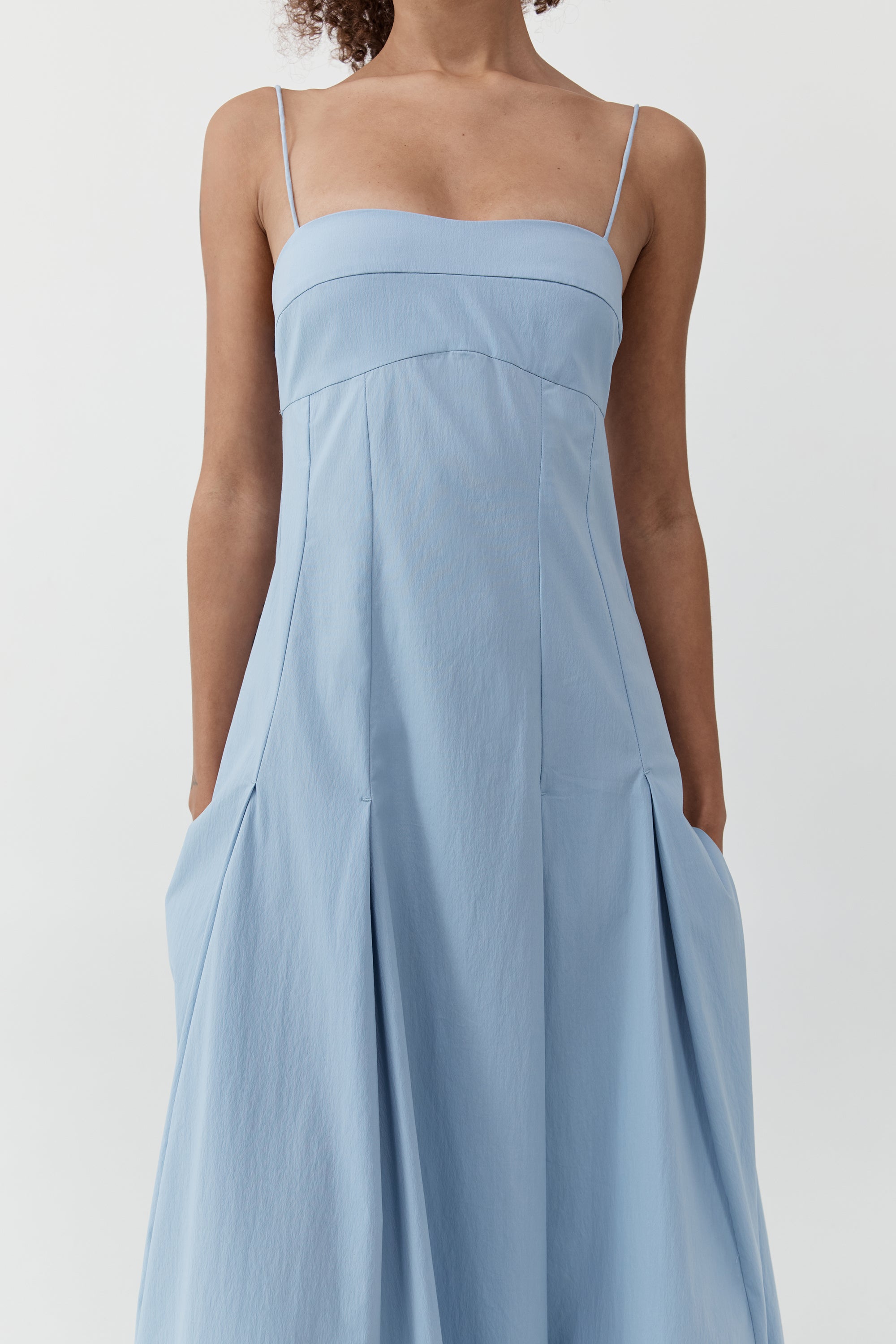 Close up of a woman wearing the st. agni everyday cotton pleated dress in sky in front of a cream background