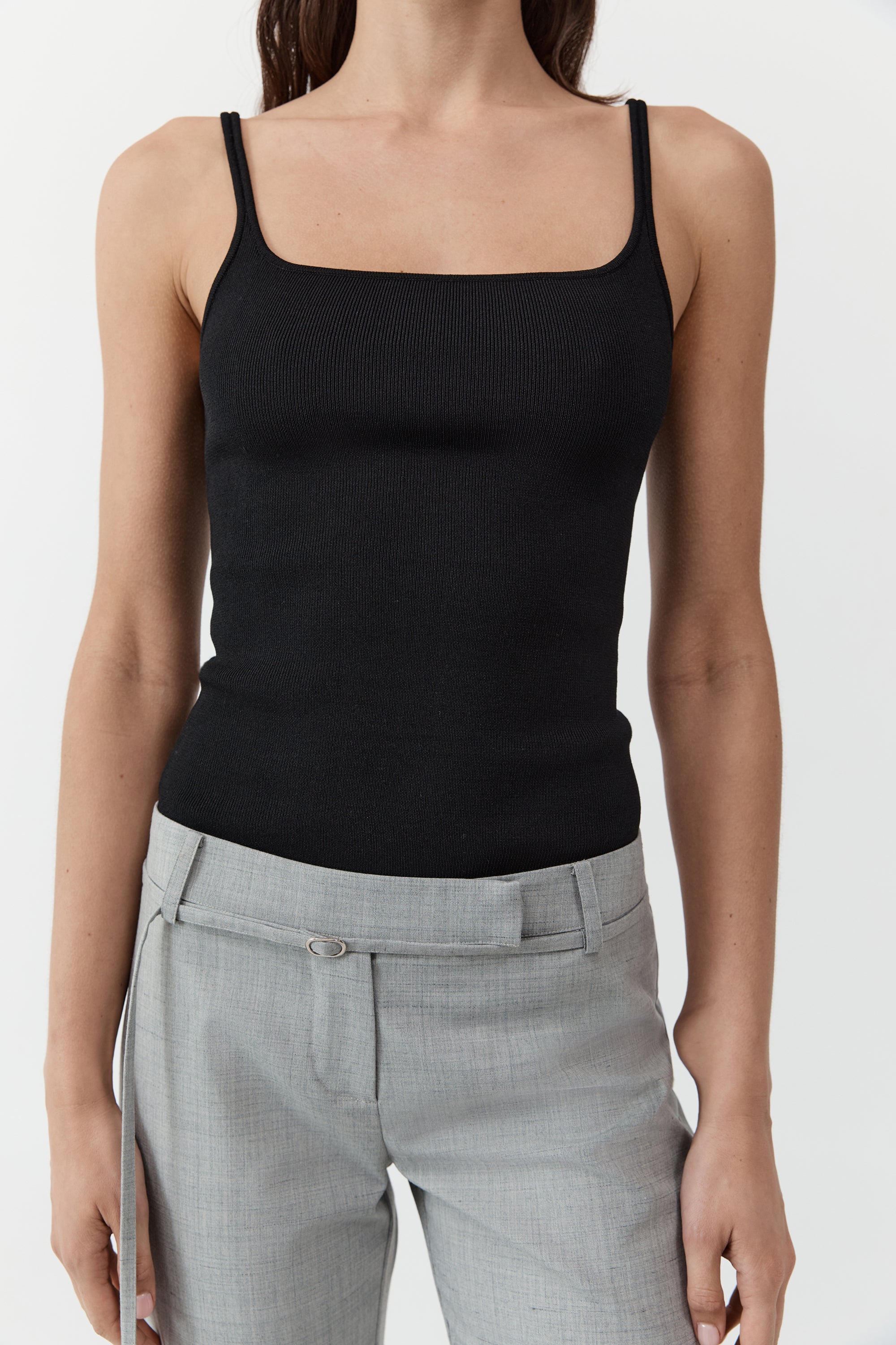 Close up of a woman wearing the st. agni slim square neck top In black with gray trousers in front of a cream background