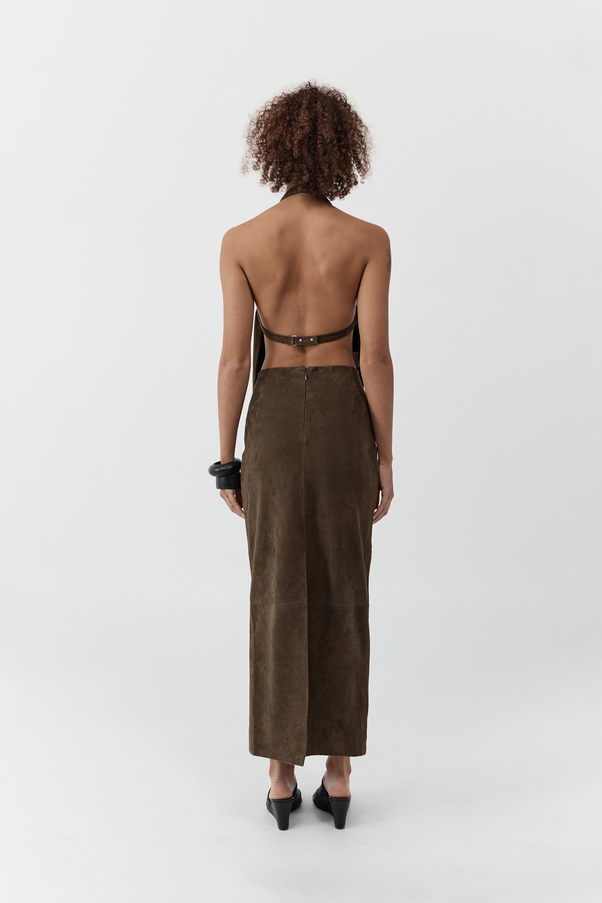 Backside of a woman wearing a st. agni suede apron top with suede skirt in front of a cream background