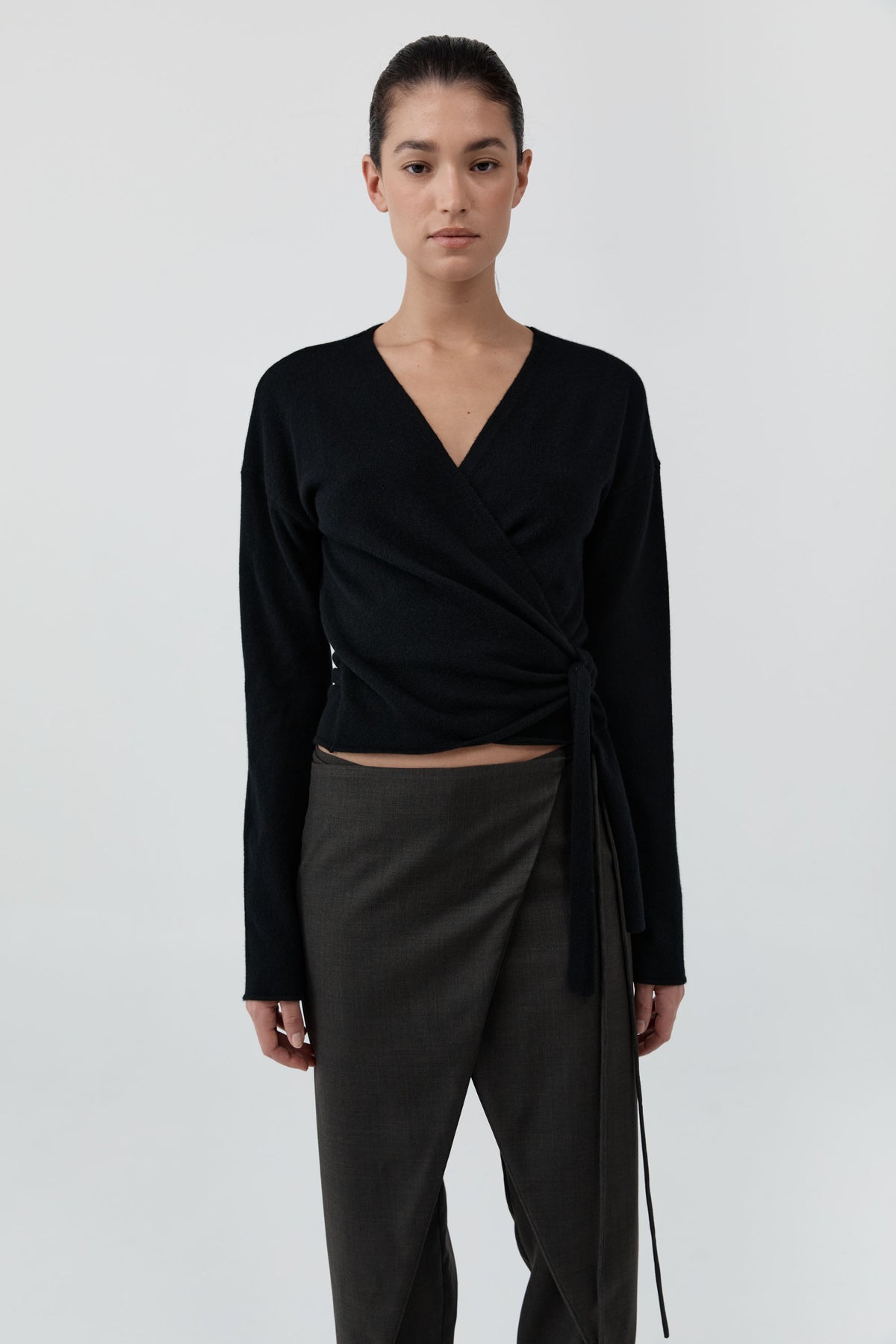 Woman wearing St Agni Baby Wool Wrap Top and gray pants standing against a white background