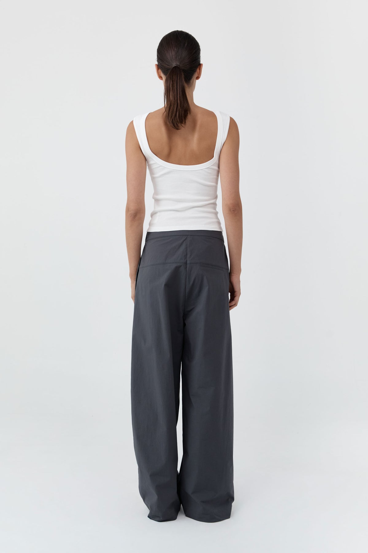 Backside of a woman wearing the St Agni Organic Cotton Ballerina Top-White and gray pants standing against a white background