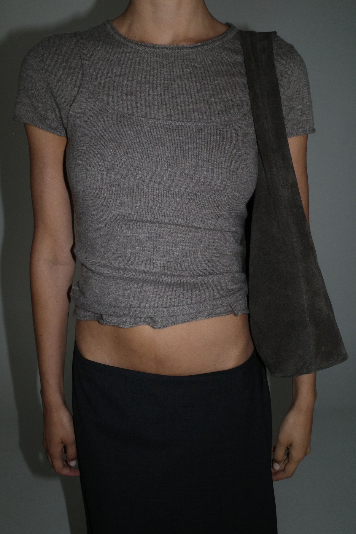 Woman wearing the St Agni Fine Merino Wool Baby Tee with a black skirt standing against a gray wall
