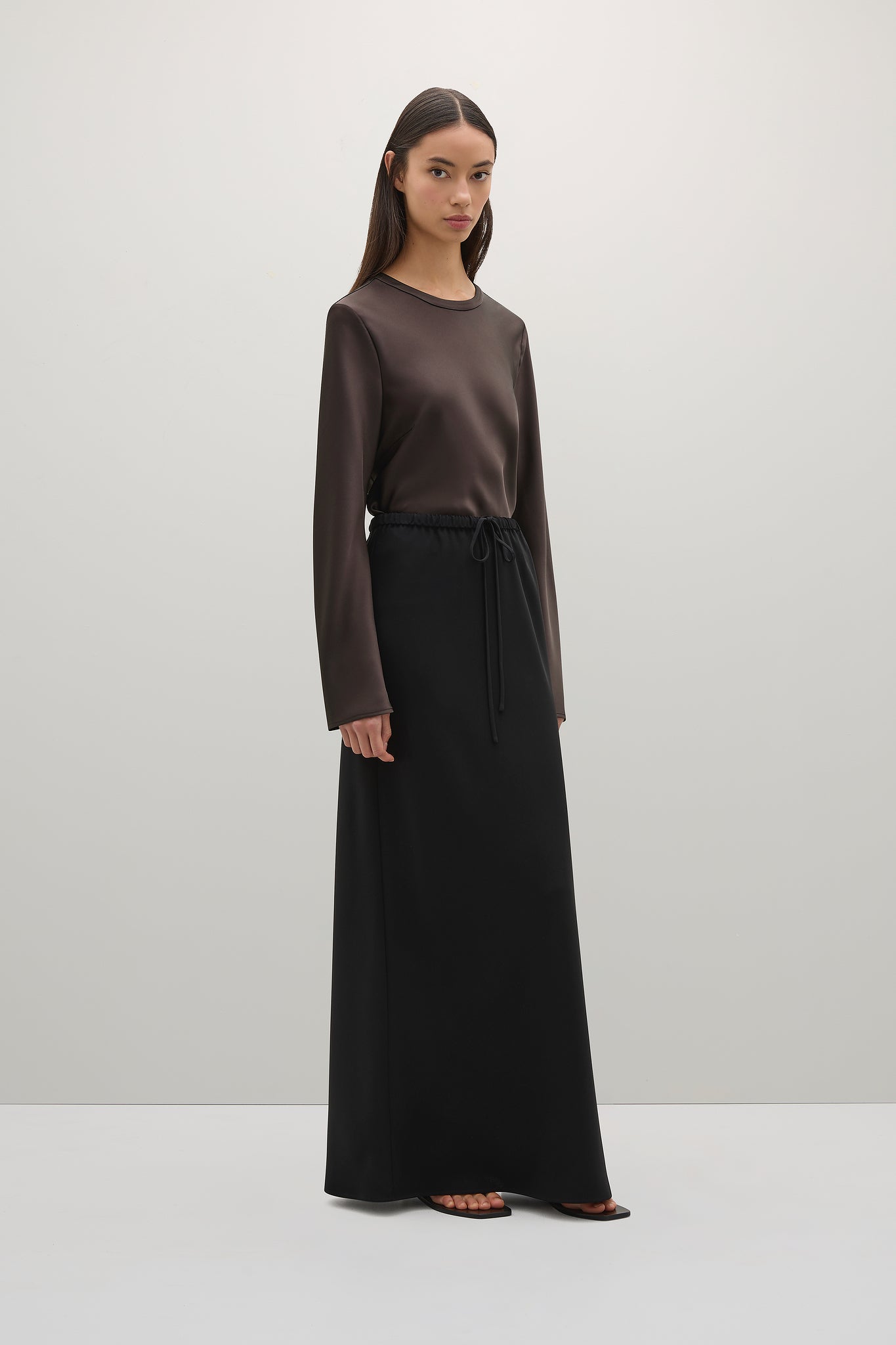 Woman wearing a brown long-sleeve top and black skirt on a white background