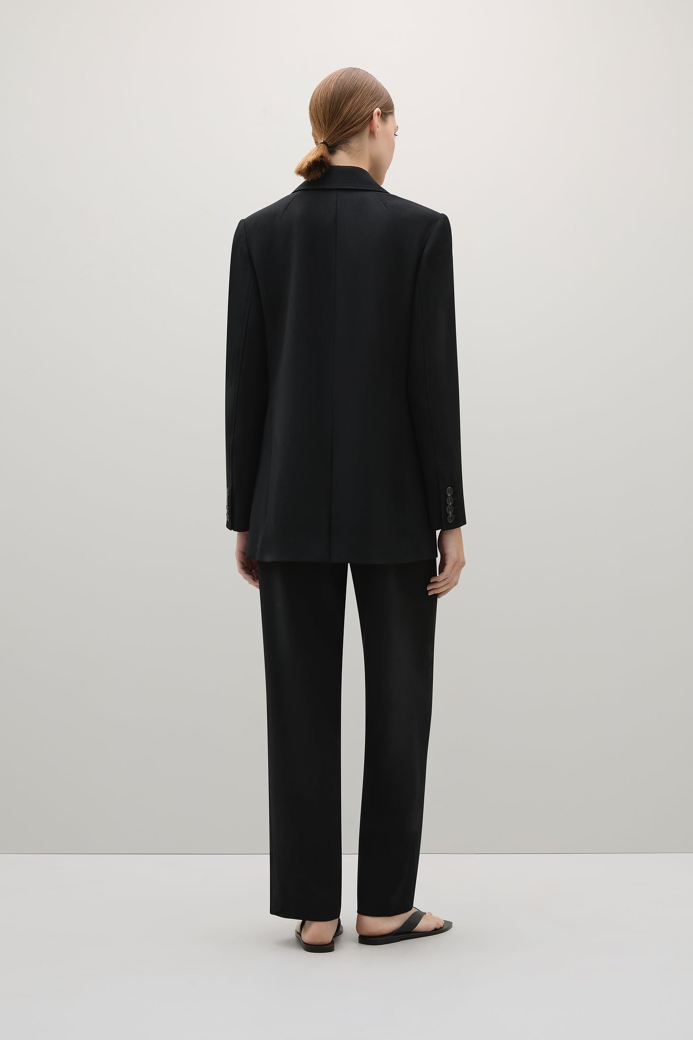 Person wearing a black suit standing against a white background