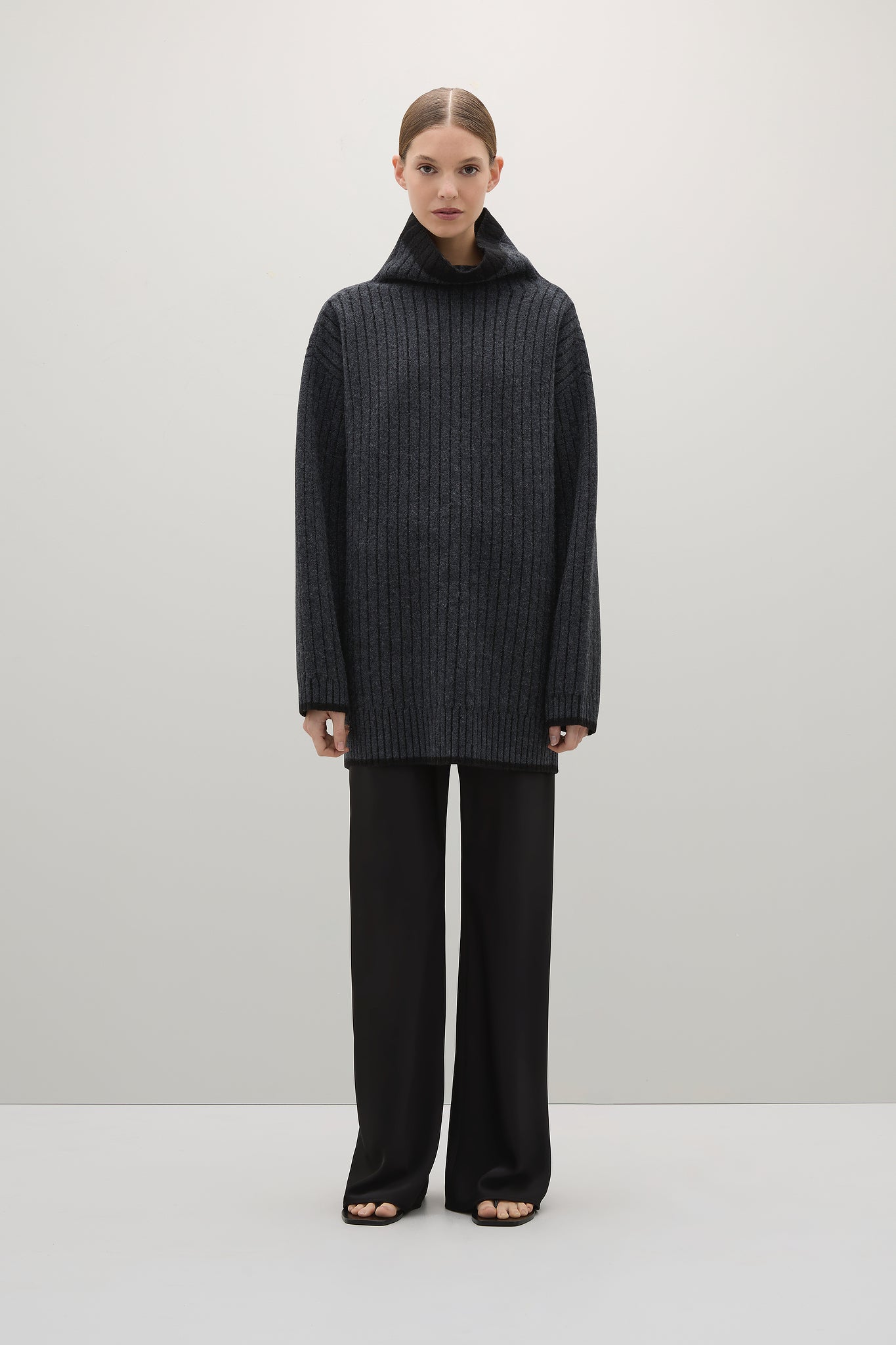 Person wearing a dark gray sweater and pants on a white background