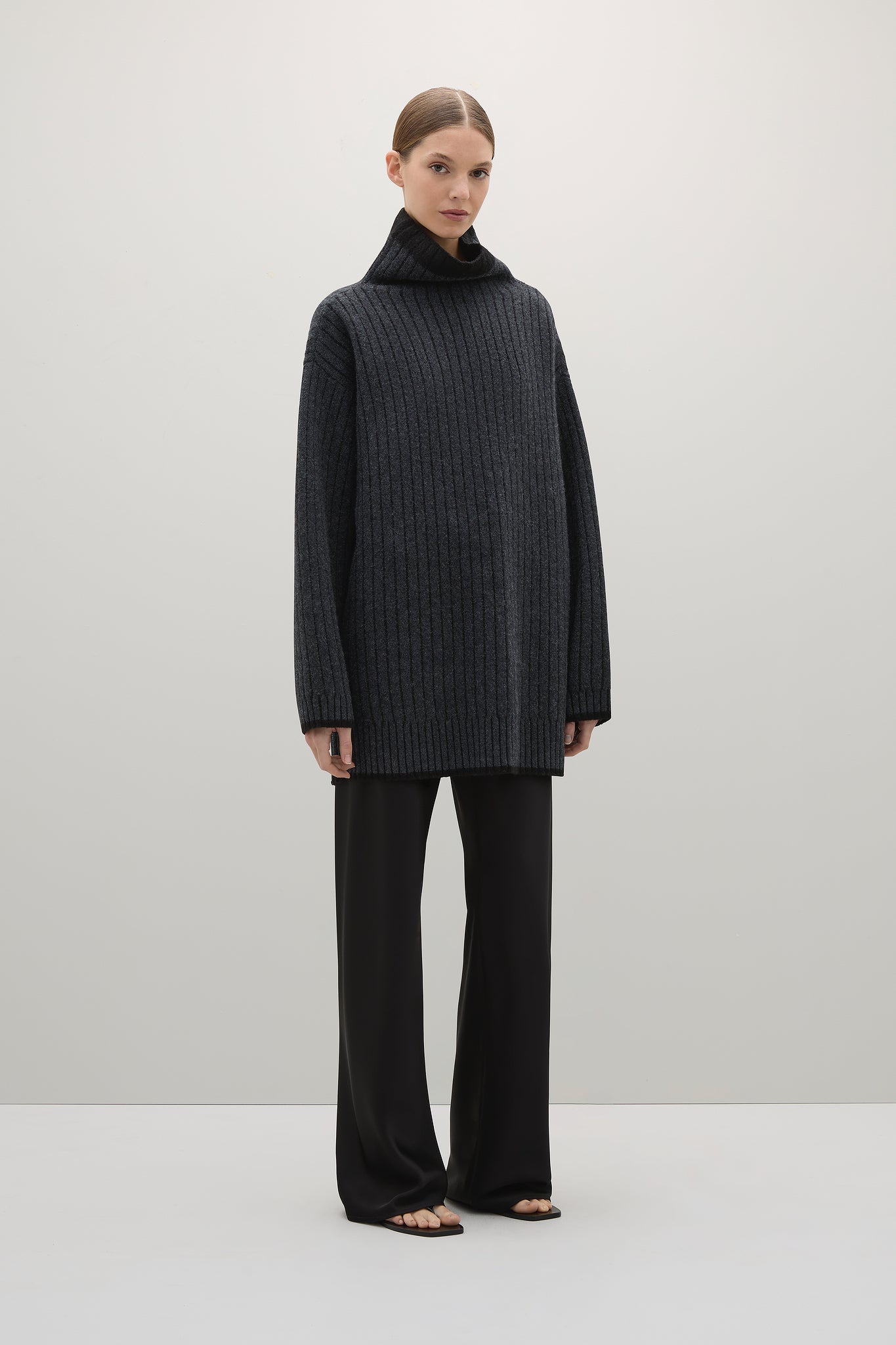 Person wearing a dark gray ribbed sweater and black pants on a white background