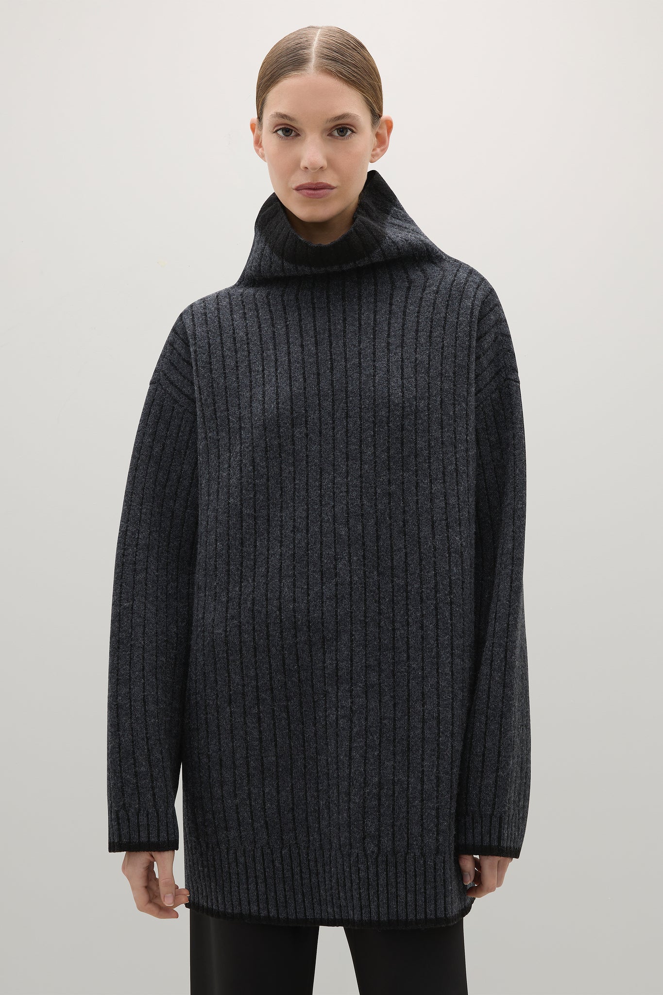 Woman wearing a dark gray ribbed sweater against a plain background