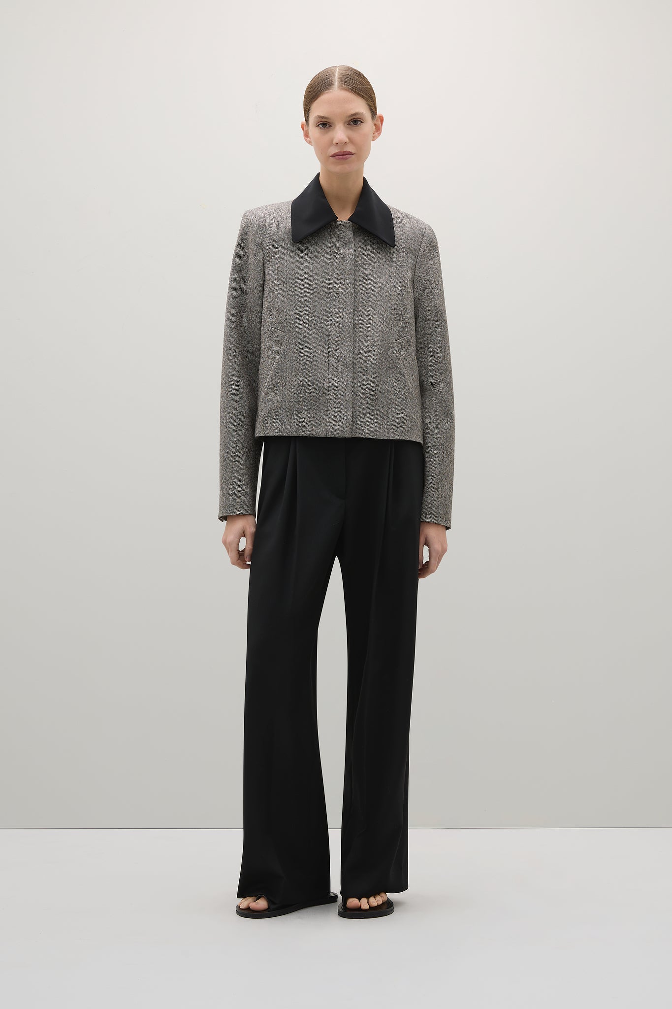 Woman wearing a gray coat with black collar and black pants on a white background
