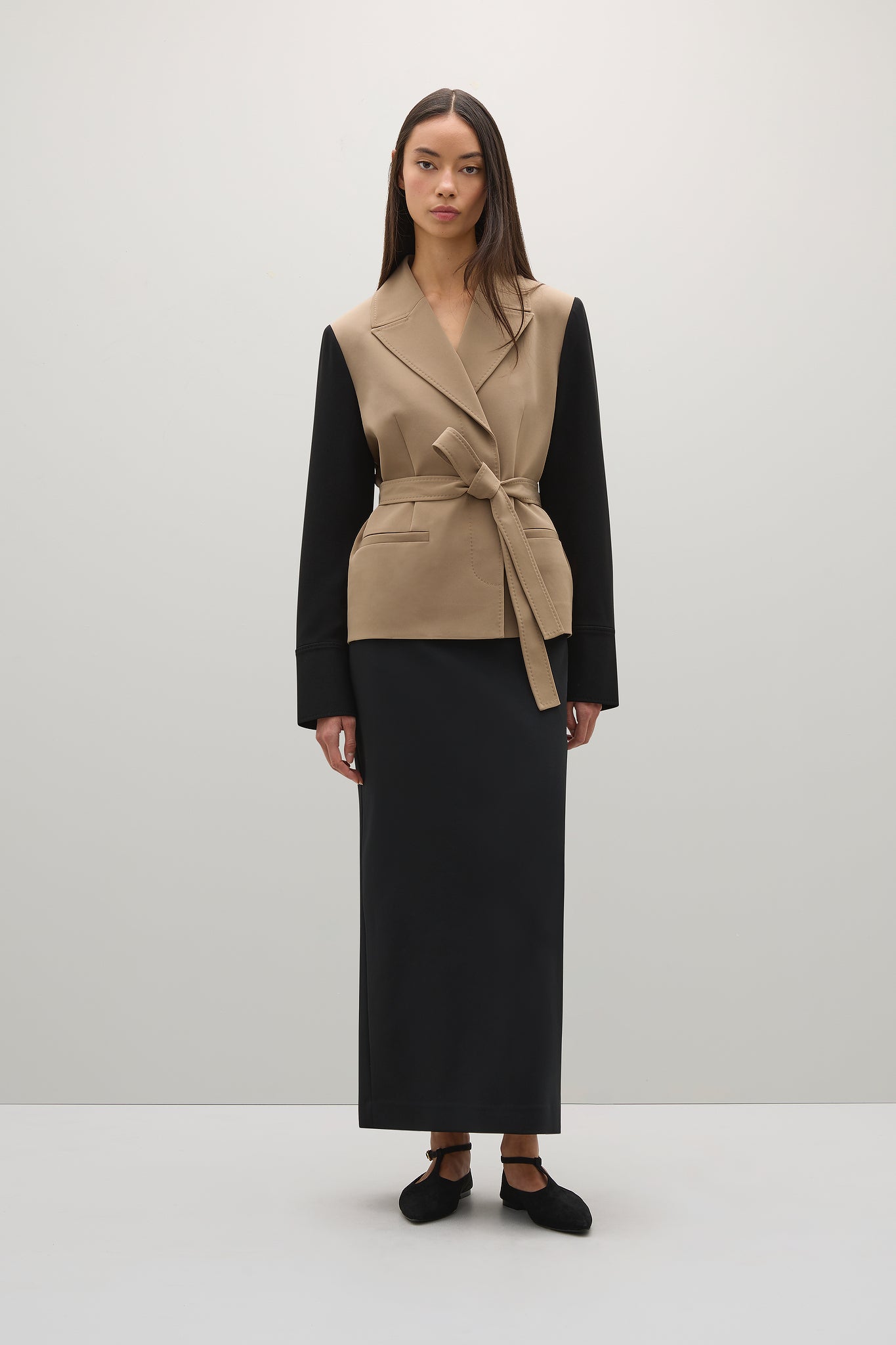 Woman wearing a beige vest over a black outfit on a white background