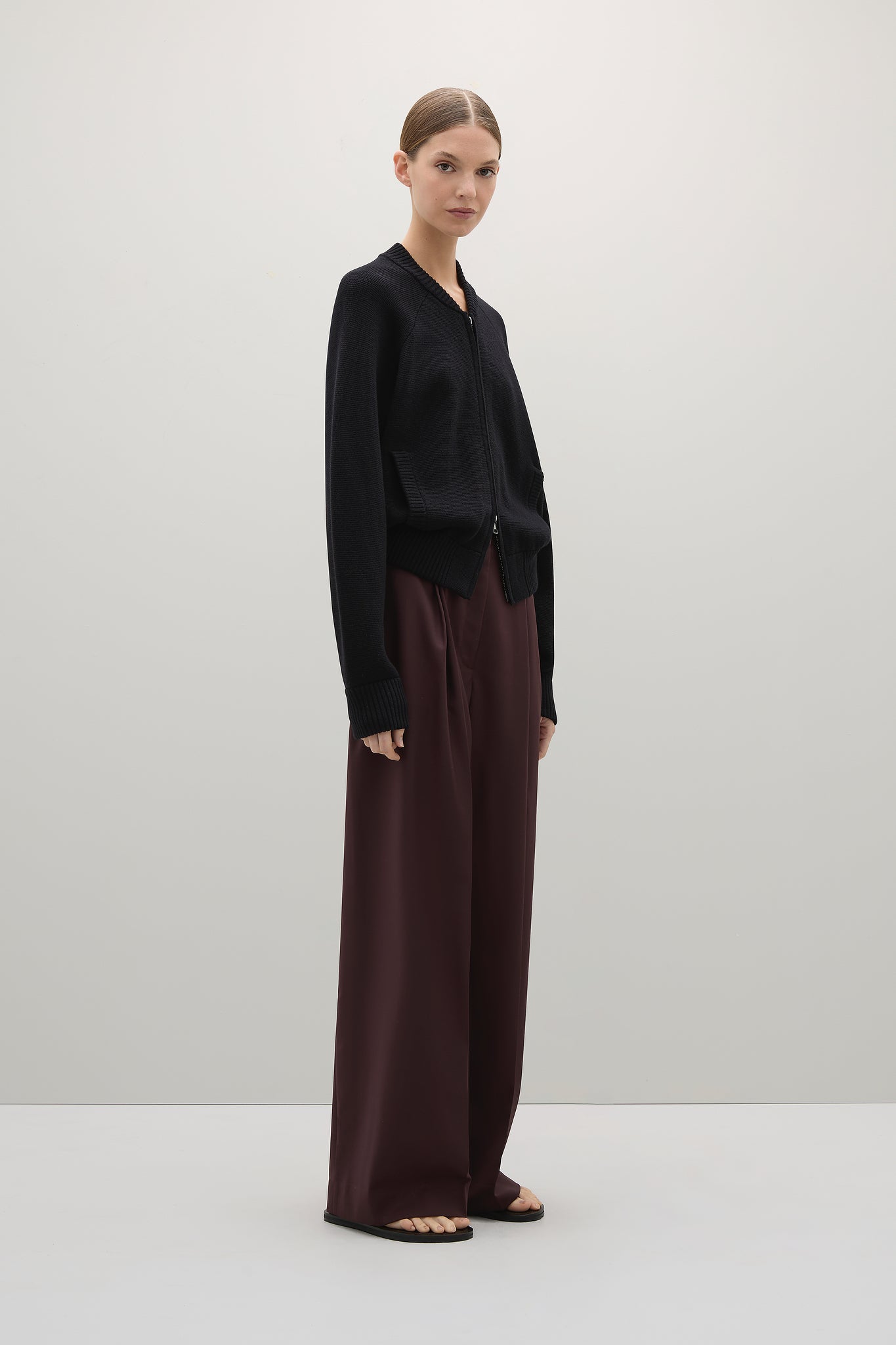 Woman wearing a black cardigan and brown pants on a white background