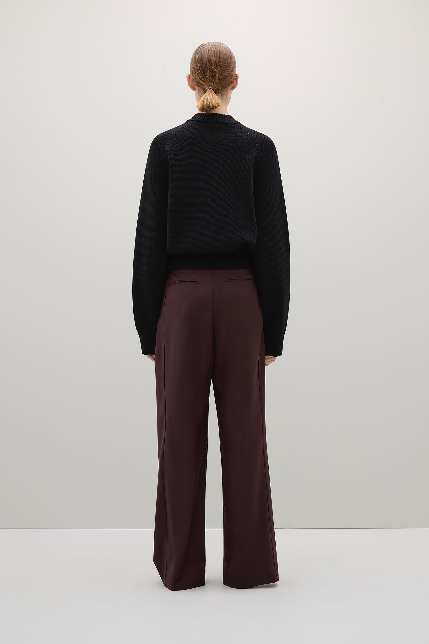 Person wearing a black sweater and burgundy pants on a white background