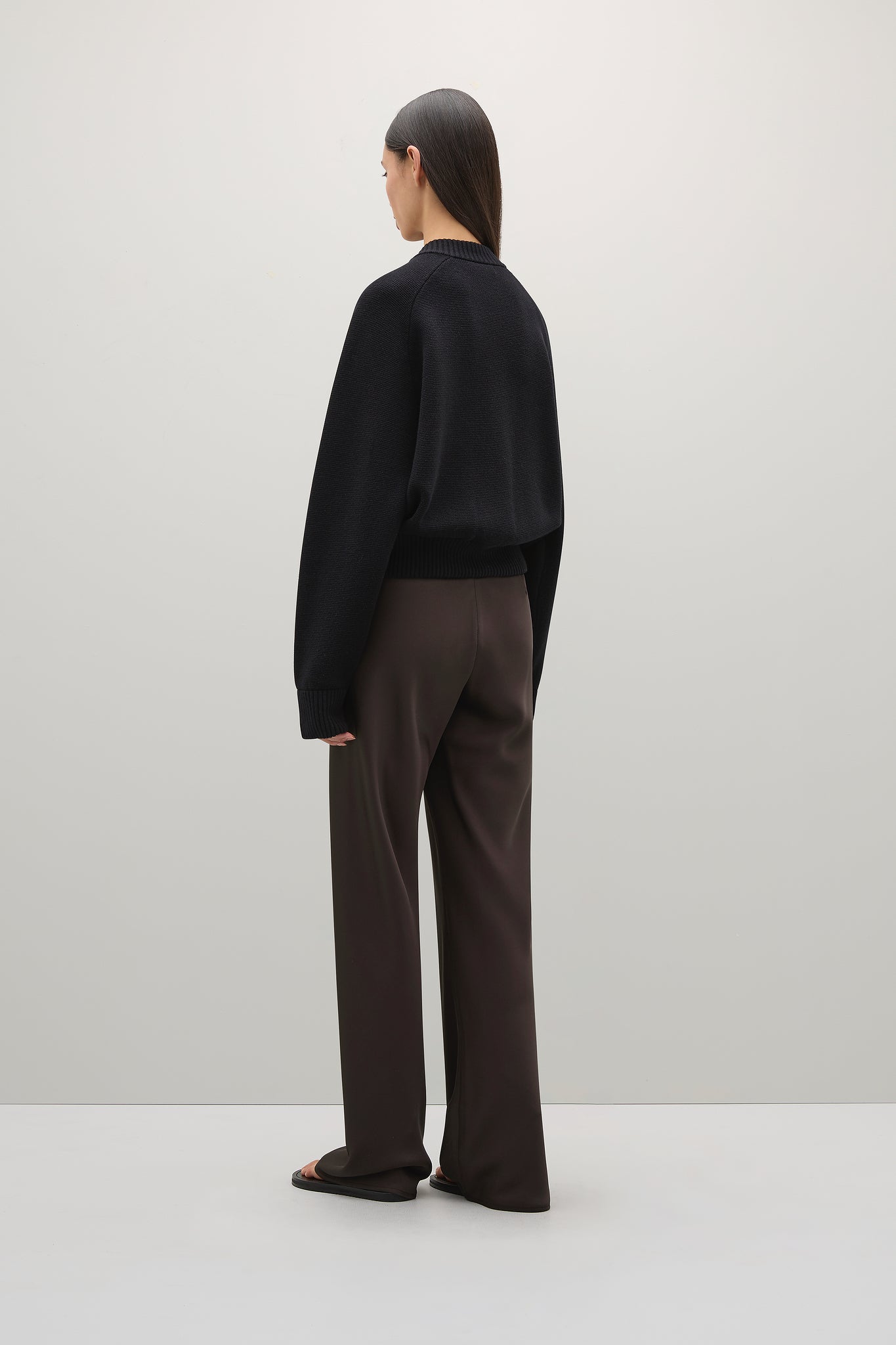 Person wearing a black sweater and brown pants on a white background