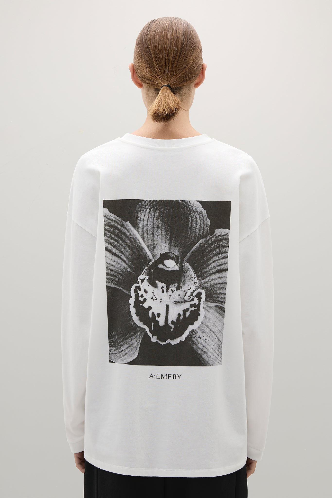 Person wearing a white sweatshirt with a black and white orchid graphic on the back, standing against a plain background.