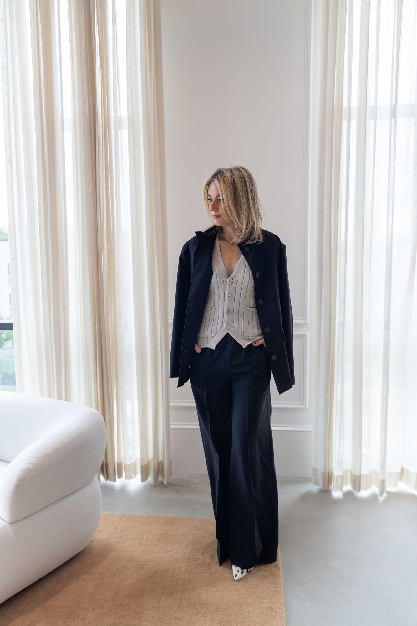 image of a woman wearing the Amo marlowe vest and house of dagmar wool overshirt and elastic trousers standing in a room with white curtains and a tan area rug.