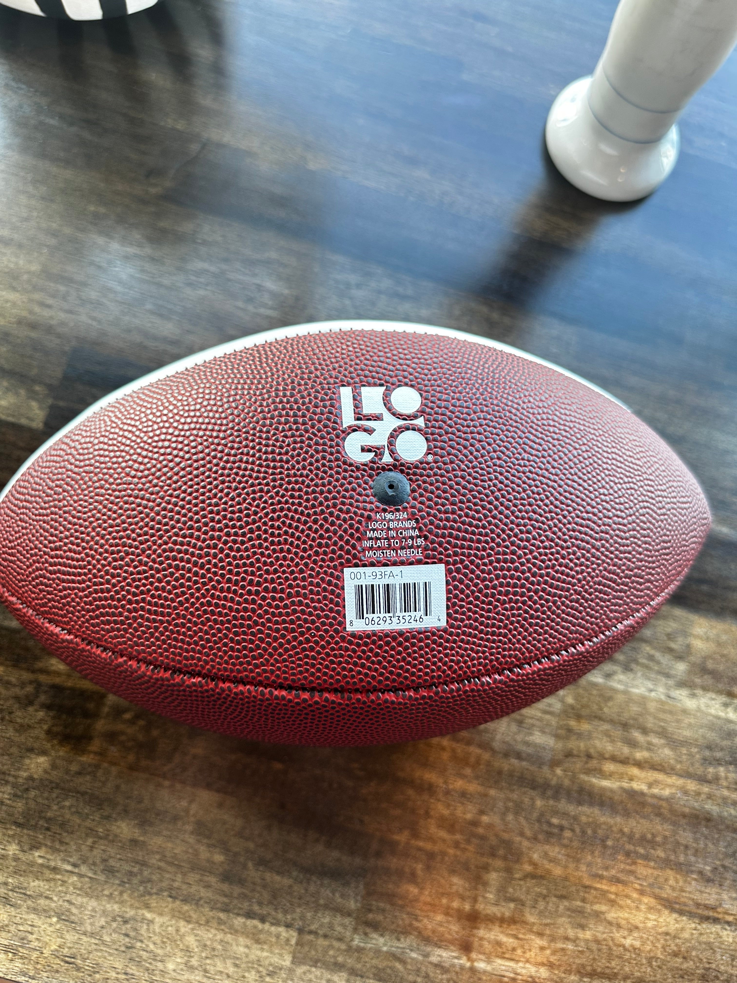 A brown textured leather football lying on a dark wooden floor, with a white sticker and barcode on the side.