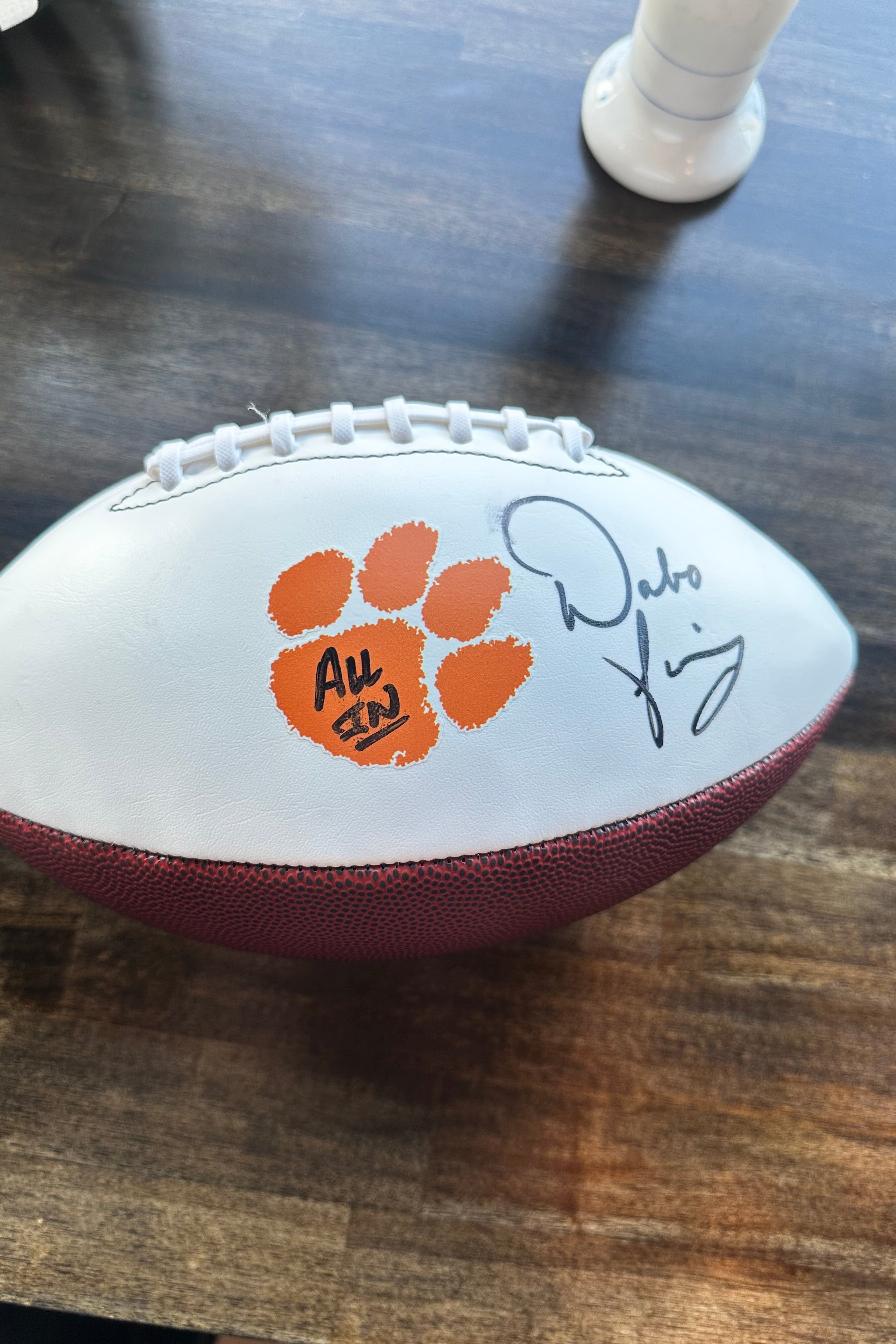 A white and brown football signed by Dabo Swinney an orange Clemson Tigers paw print and 'All 2022' stamp, resting on a dark wooden table.