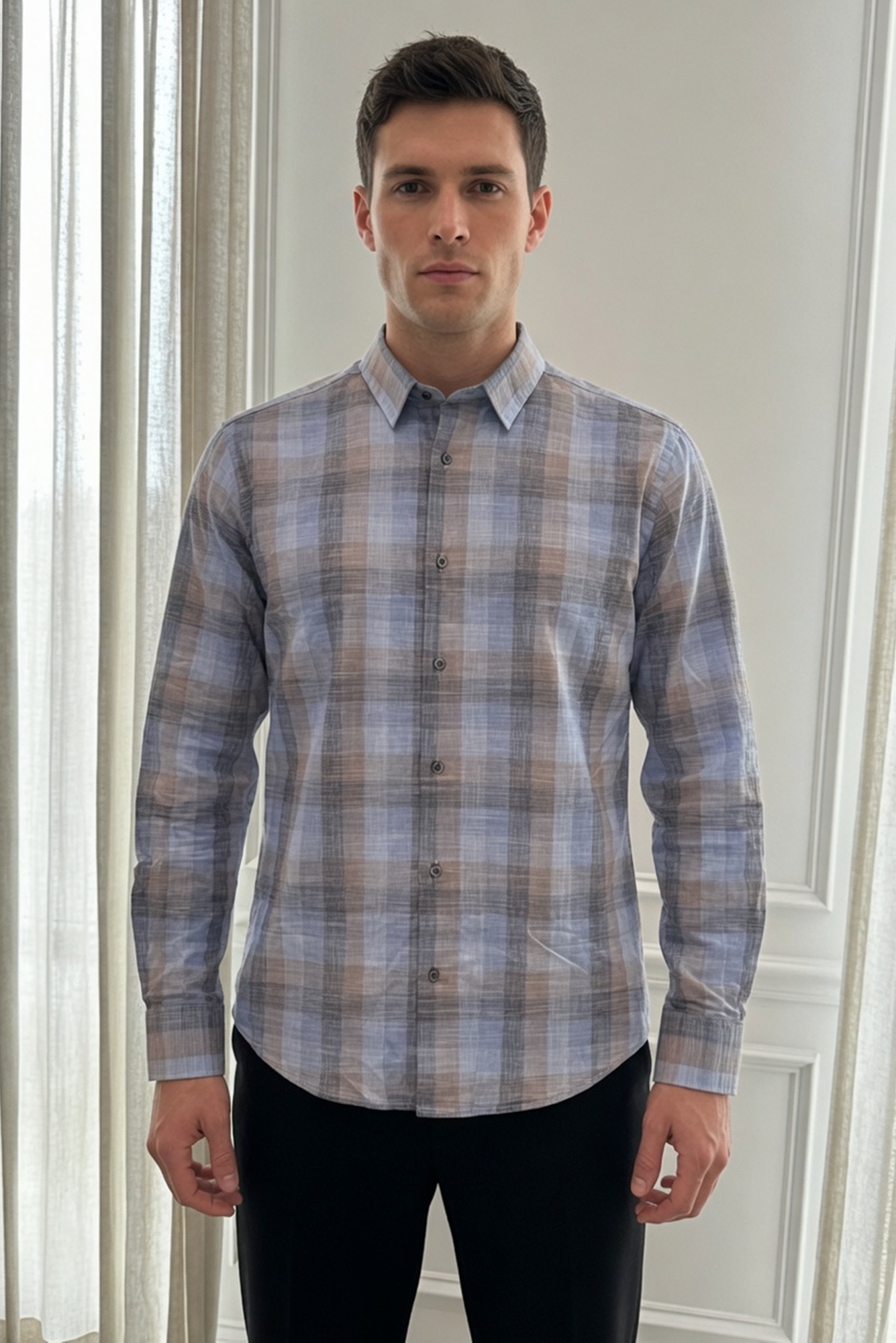 Man wearing a plaid shirt standing in front of a white wall.