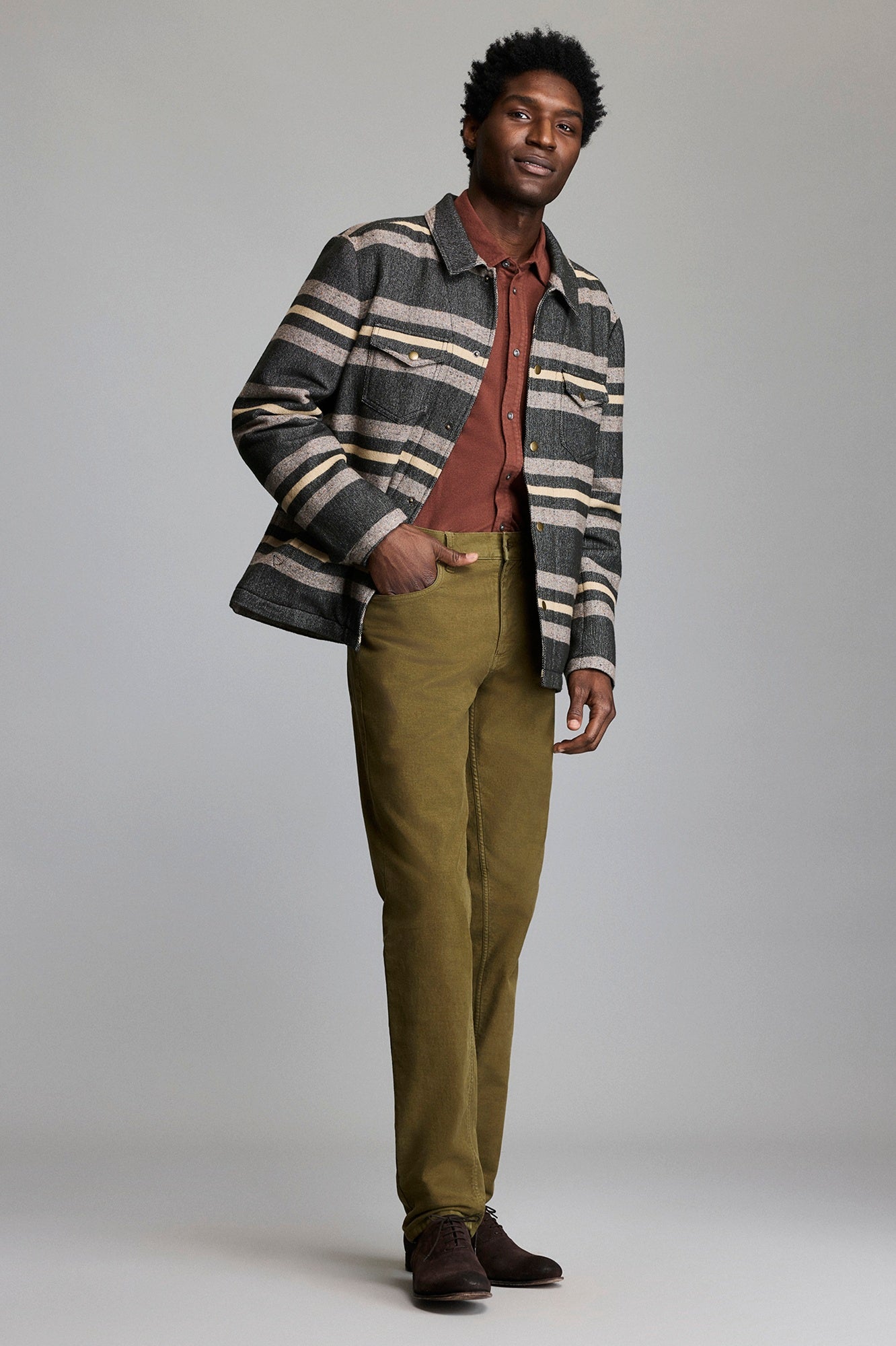 Man wearing a striped jacket, red shirt, and green pants on a plain background