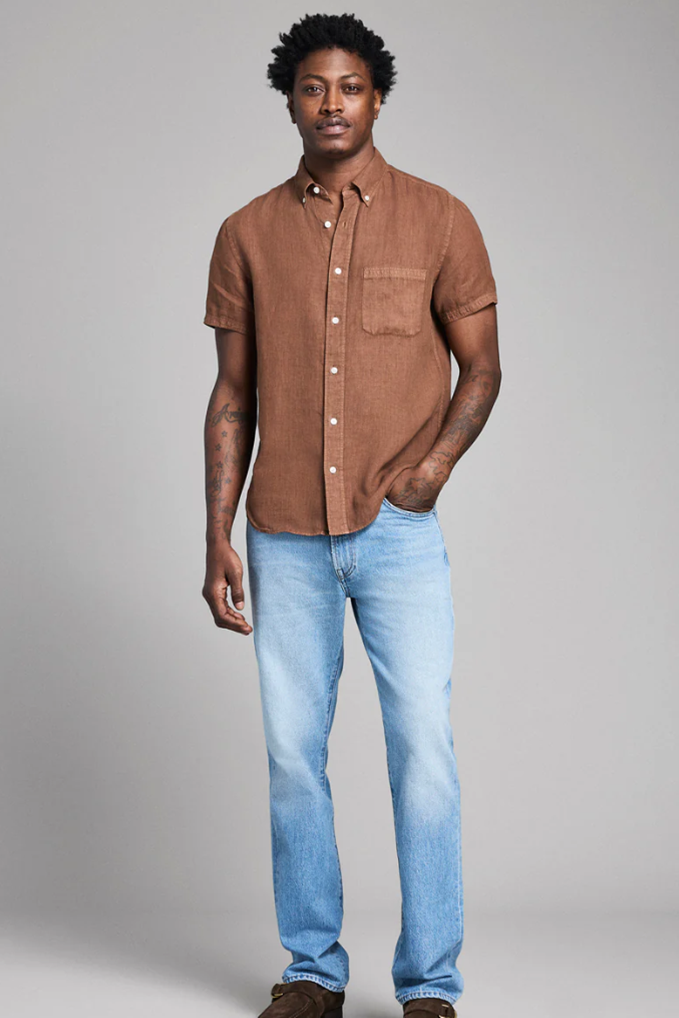 Man wearing a brown shirt and blue jeans against a gray background