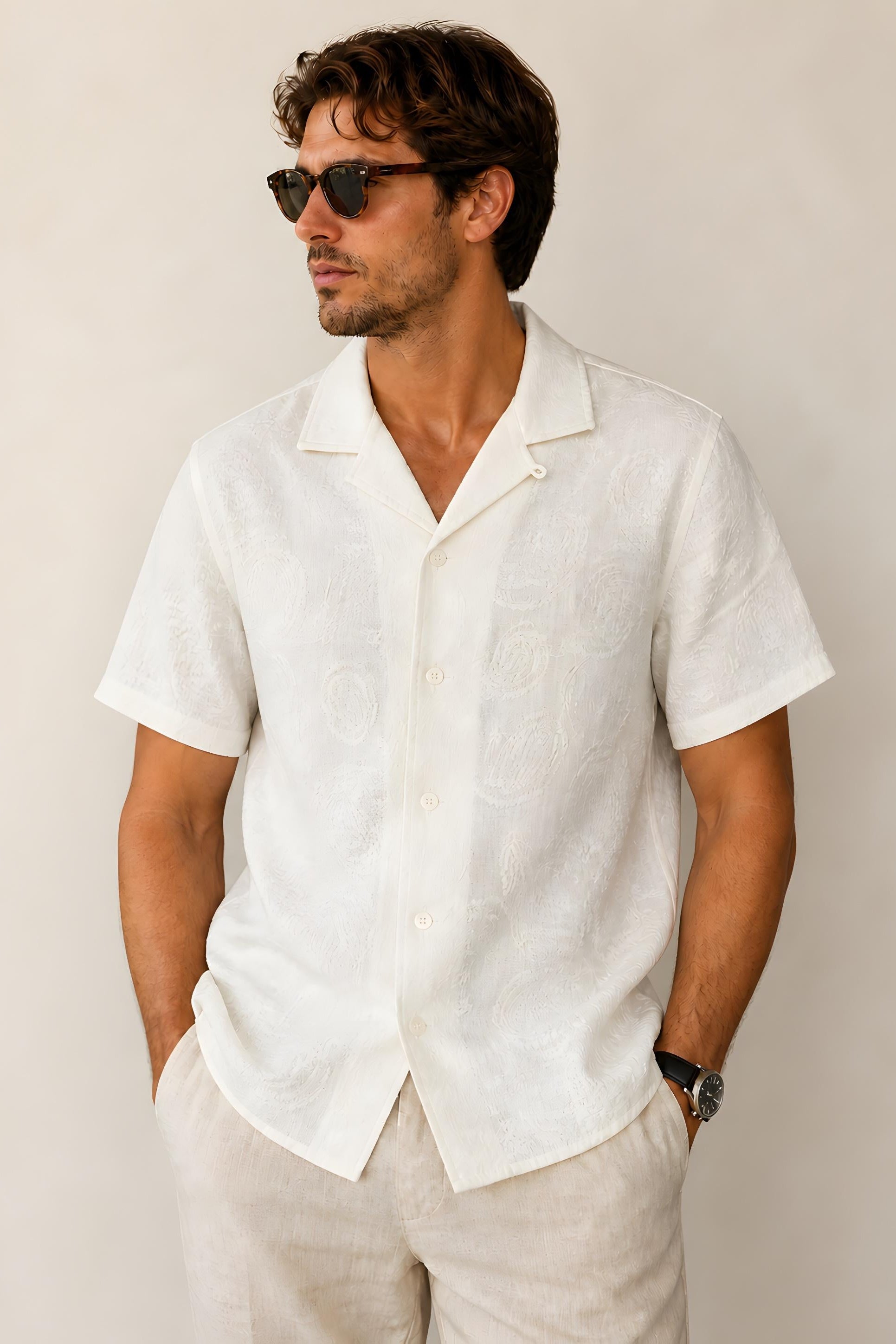 Man wearing a white short-sleeve shirt and sunglasses against a plain background