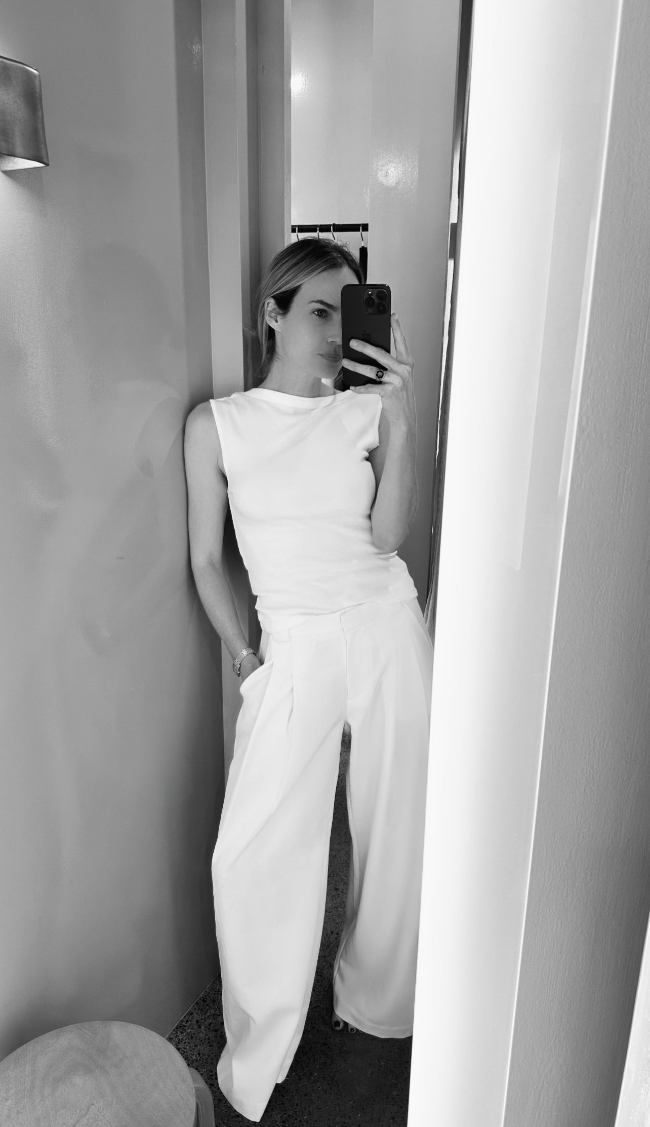 Person wearing a white outfit taking a mirror selfie in a minimalistic room.