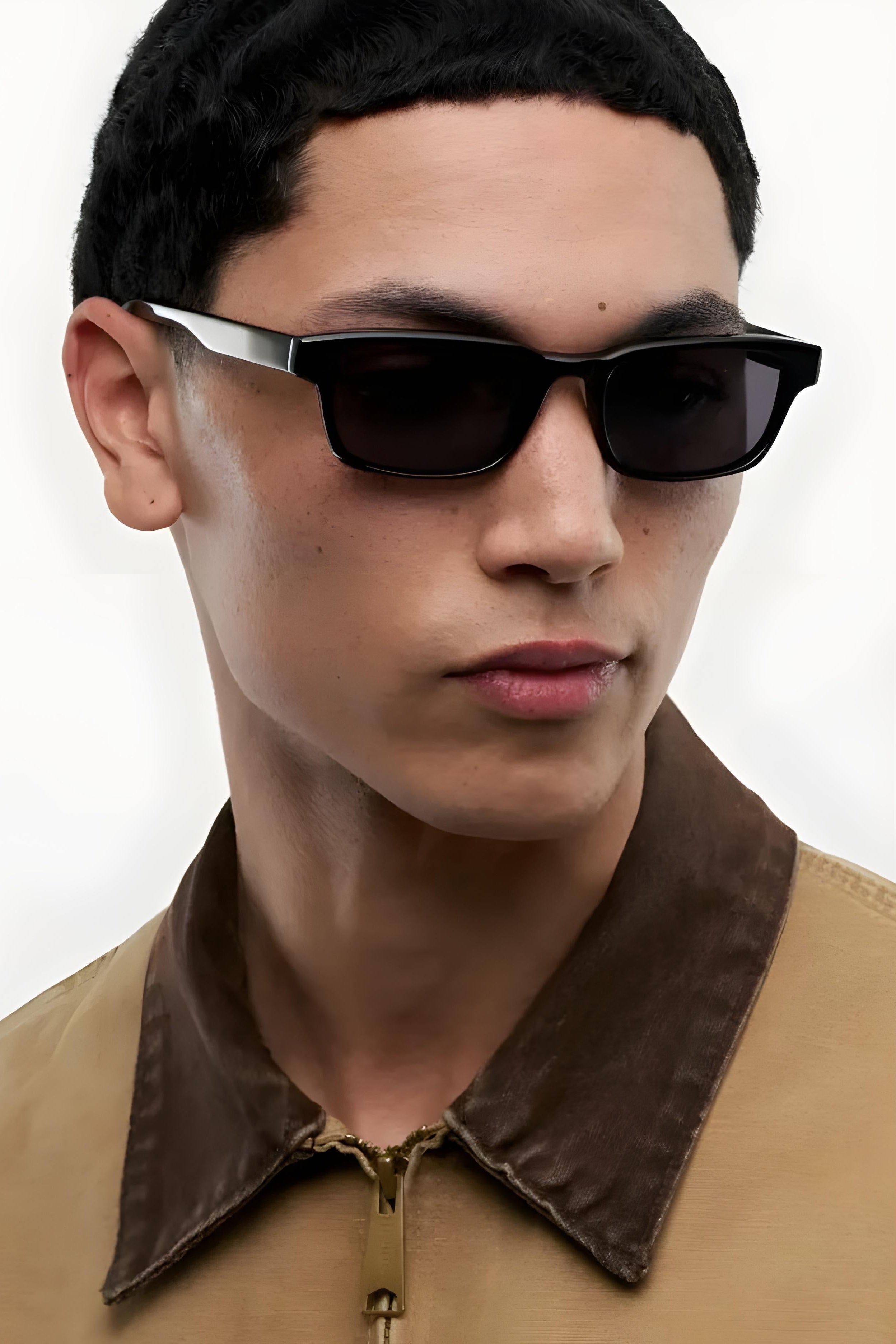 Person wearing black sunglasses and a brown jacket on a white background