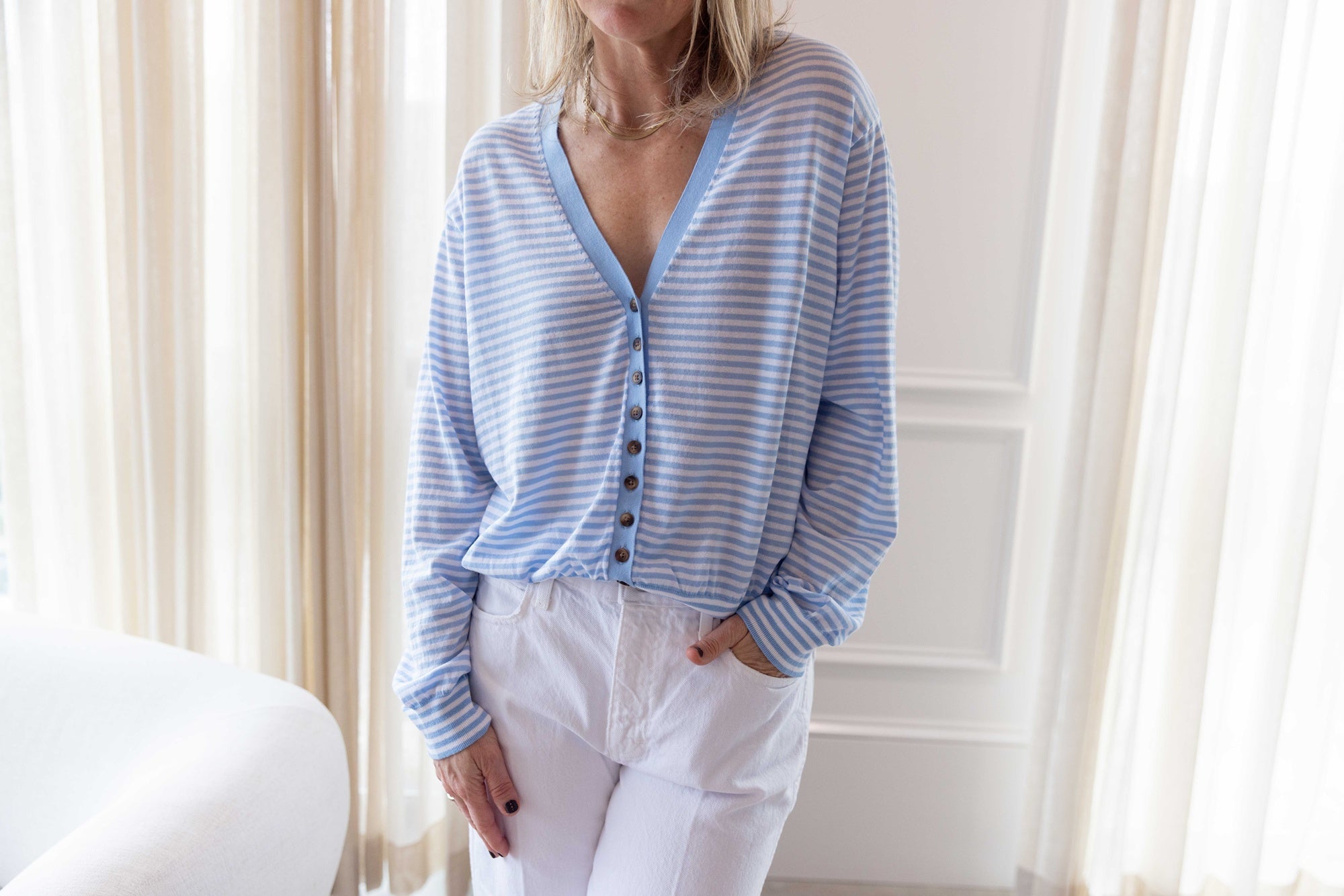 Close up of a woman wearing the ciao lucia jorgie cardigan standing in a room with white curtains.