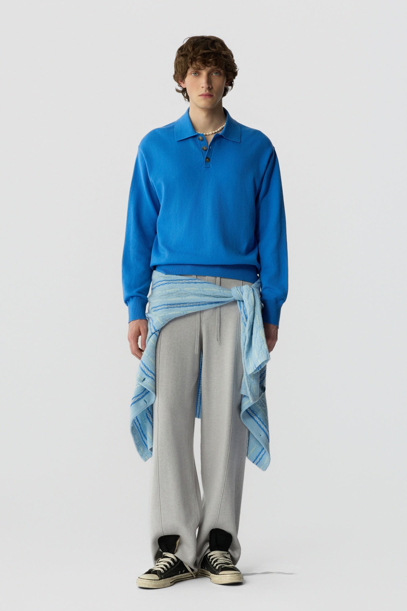 Person wearing a blue sweater and gray pants on a white background