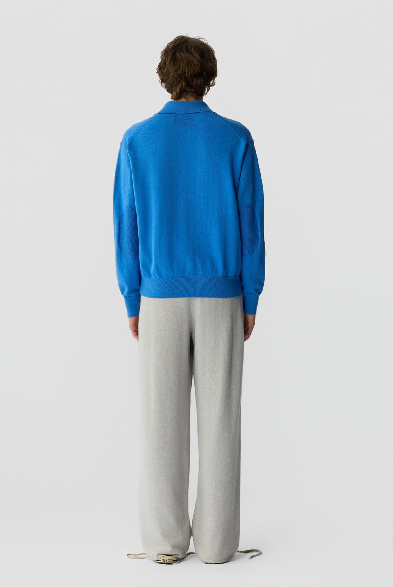 Person wearing a blue sweater and light gray pants on a white background