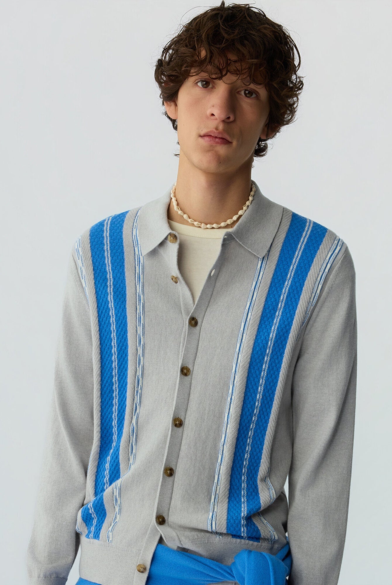 Man wearing a gray cardigan with blue stripes on a white background