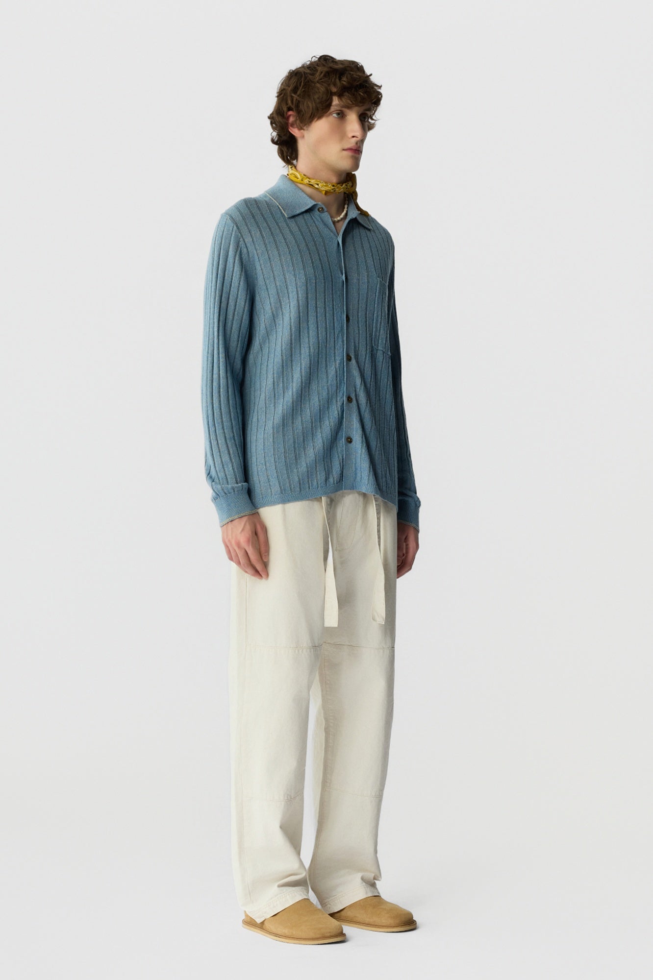 Man wearing a blue textured shirt and beige pants on a white background