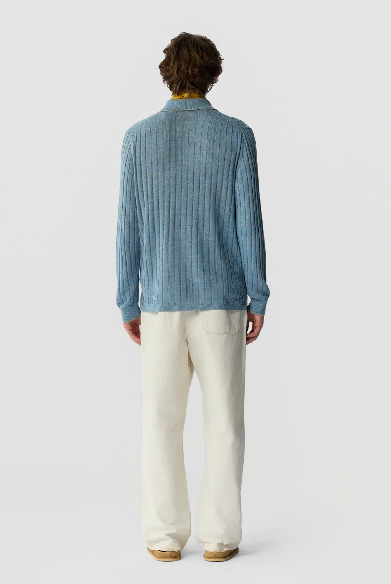 Person wearing a blue ribbed shirt and white pants on a light gray background