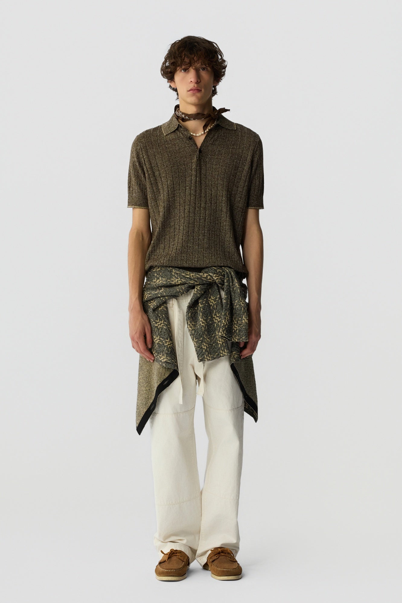 Man wearing a patterned shirt and white pants on a plain background