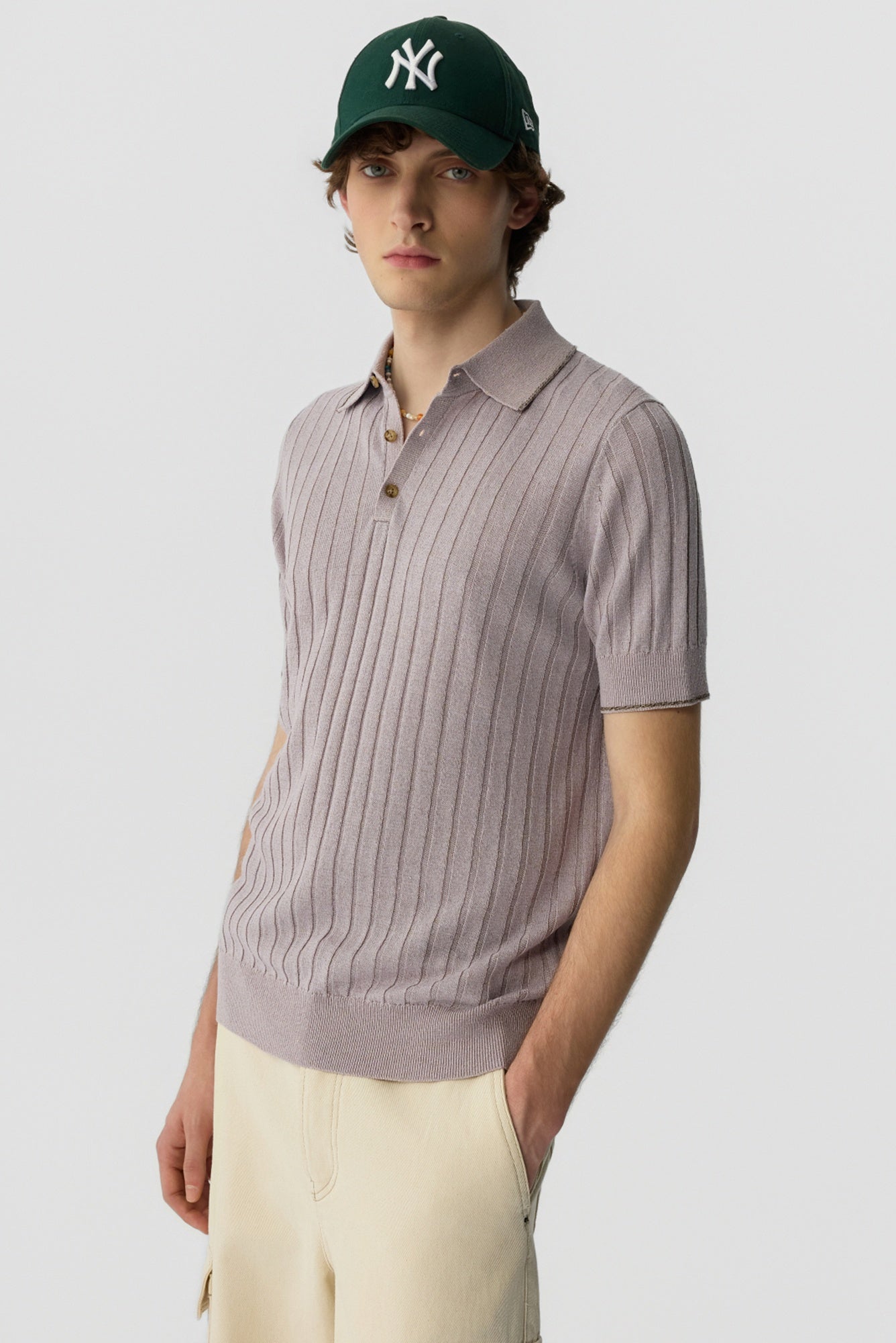 Man wearing a ribbed polo shirt and green cap on a light gray background
