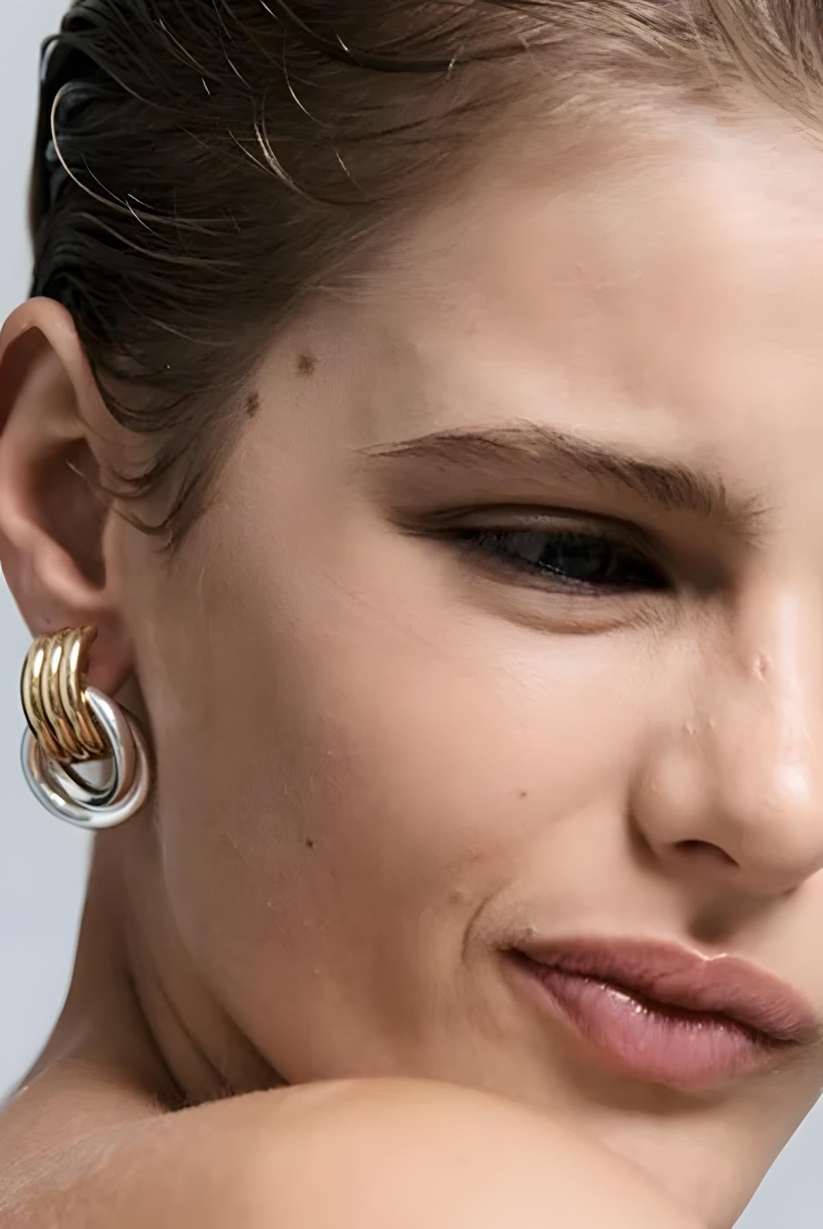 Close-up of a woman wearing gold hoop earrings with a neutral background