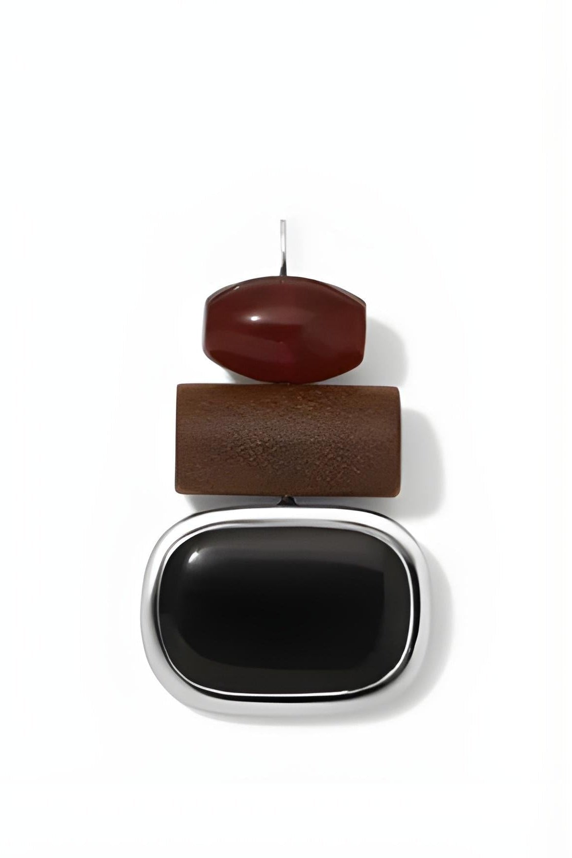 A single drop earring with stacked organic-shaped stones: a small dark red top stone, a medium brown middle stone, and a large black bottom stone set in a silver-toned frame, shown on a white background.