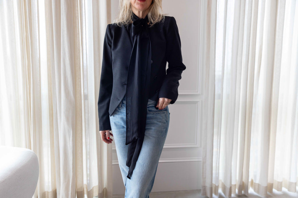 Dagmar Chiffon Scarf Blouse in black viscose, worn under a black cropped jacket with light-wash denim