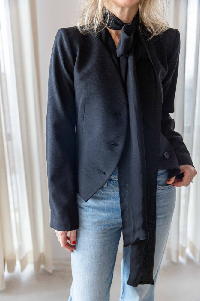 Dagmar Chiffon Scarf Blouse in black viscose, scarf tie falling under a black curved-hem jacket with light-wash denim