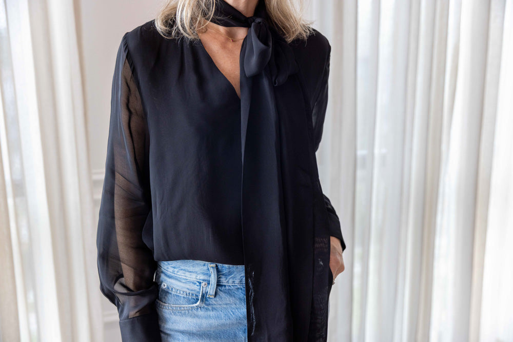 Dagmar Chiffon Scarf Blouse in black viscose, worn front view with the scarf collar open over light-wash denim