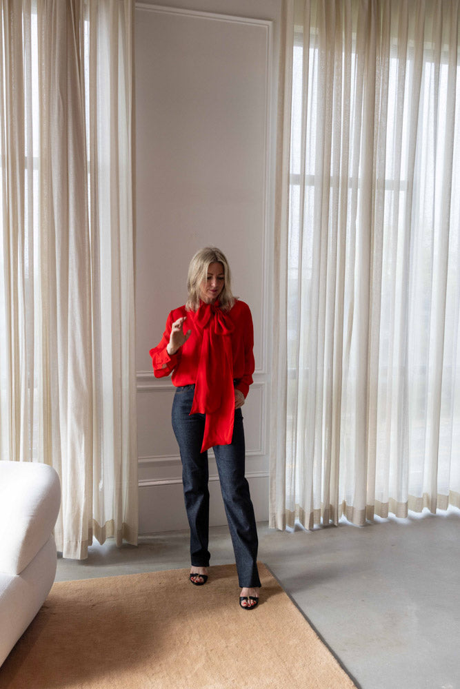 Dagmar Chiffon Scarf Blouse in red viscose, worn full length with dark straight-leg denim in a sunlit room