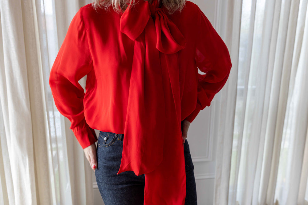 Dagmar Chiffon Scarf Blouse in red viscose, worn front view with hand in pocket and the long scarf tie loose