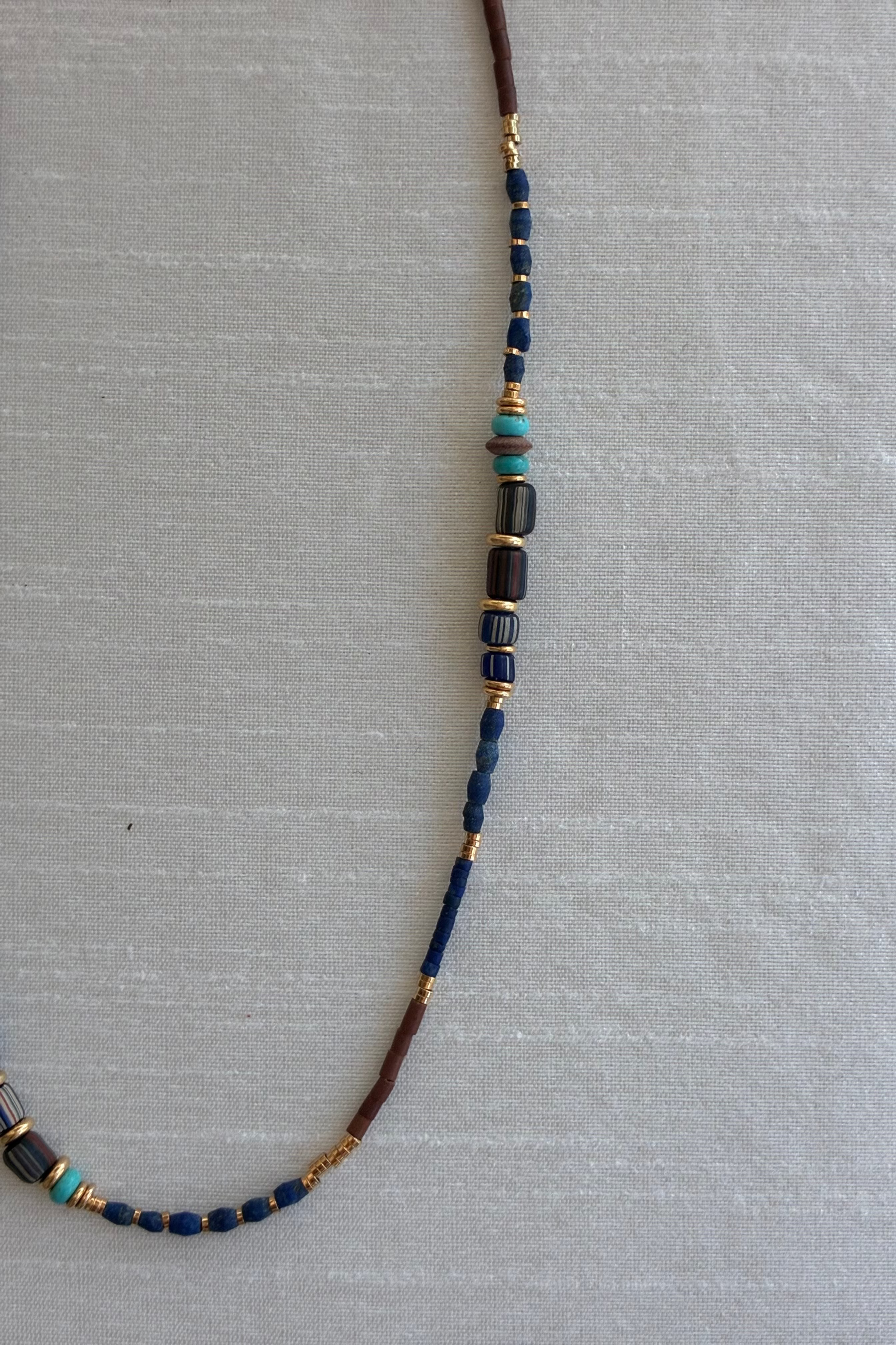 Close up image of a Gachon Pothier beaded necklace with blue and brown beads and 18kt gold plated hardware on a light gray background.