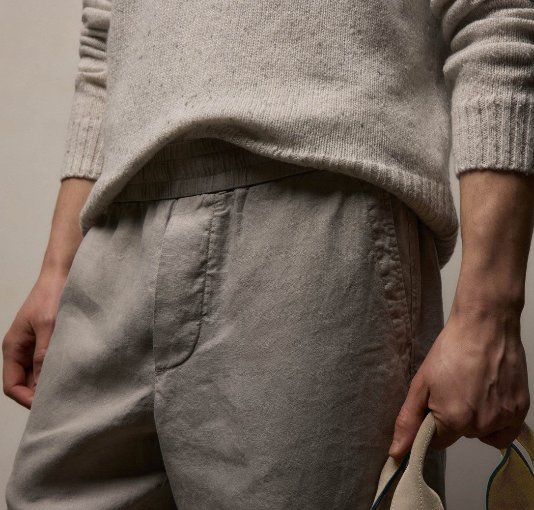 Person wearing a beige sweater and light brown pants against a neutral background