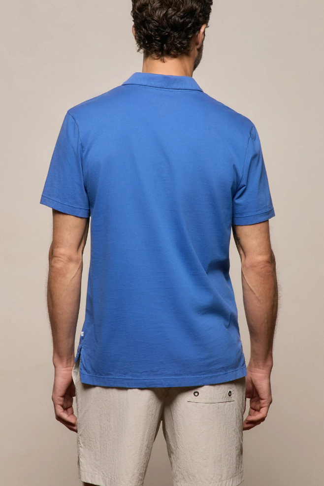 Man wearing a blue polo shirt and beige pants against a beige background
