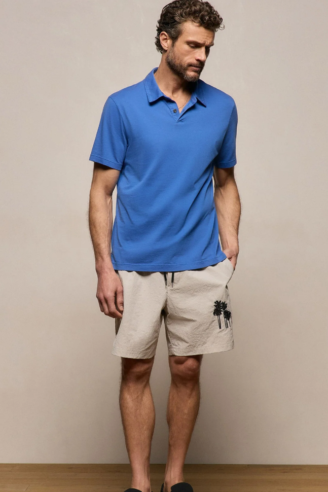 Man wearing a blue polo shirt and beige shorts against a plain background