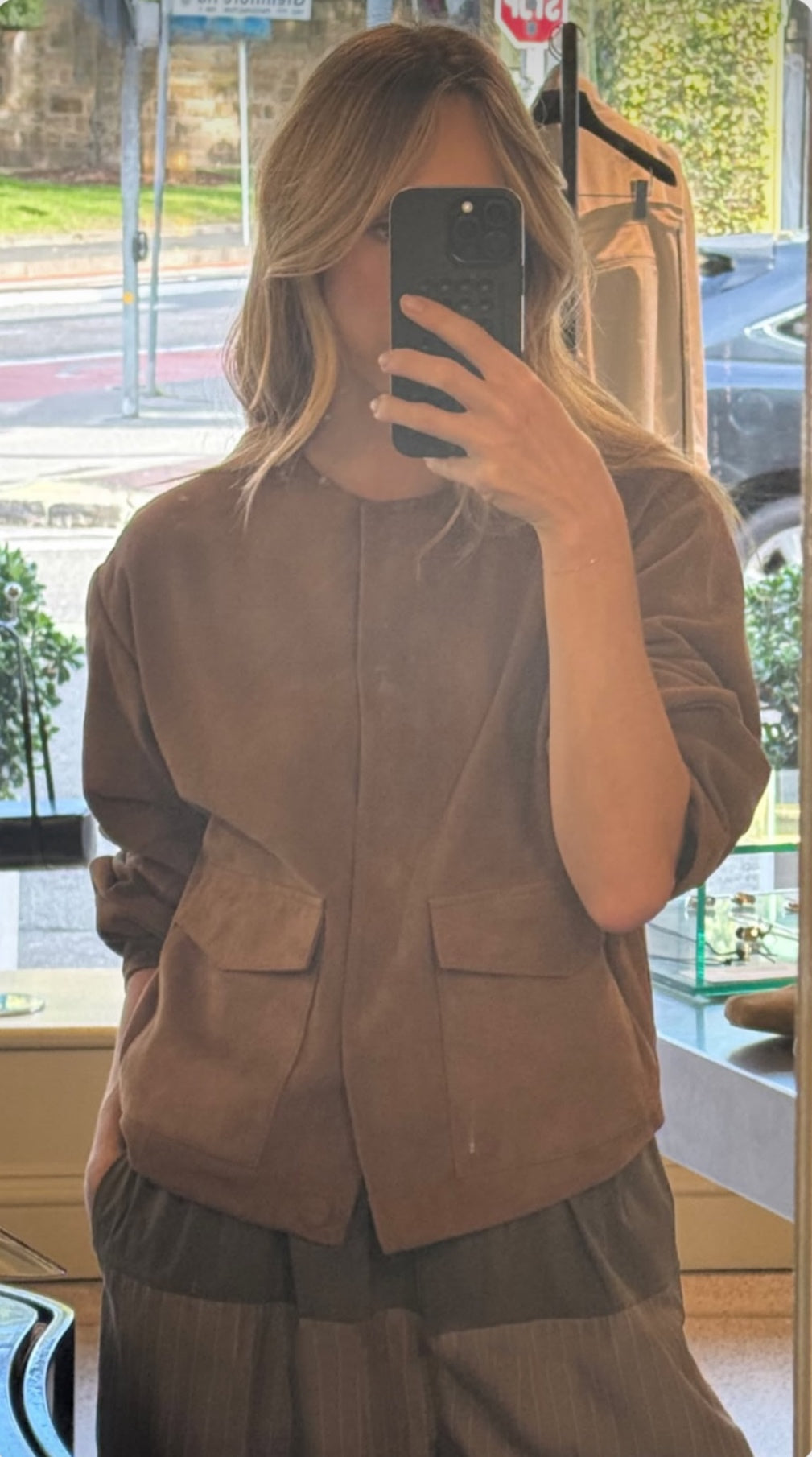 Person wearing a brown jacket taking a mirror selfie.