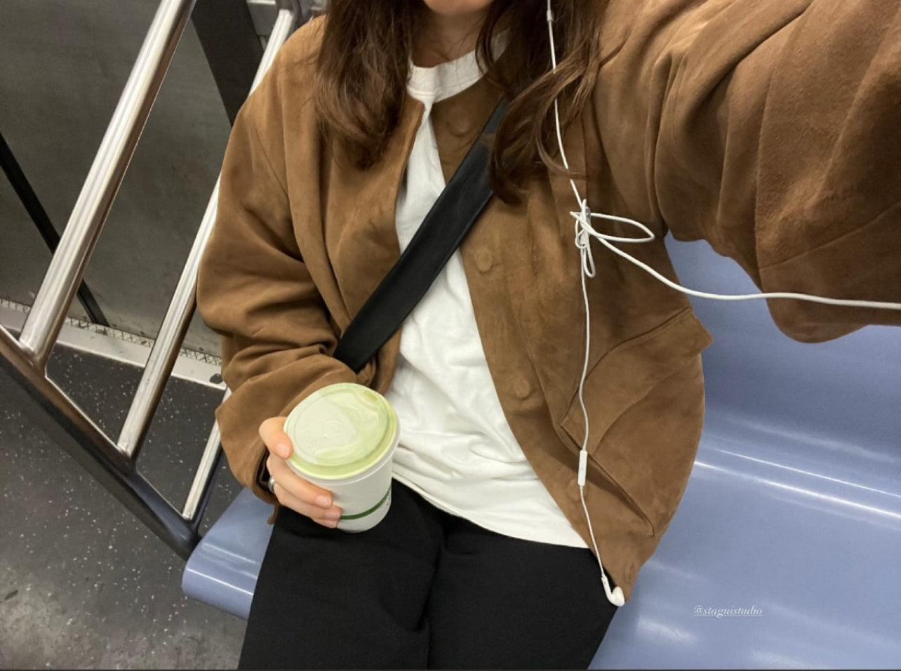 Person holding a coffee cup with earphones, standing on a staircase.