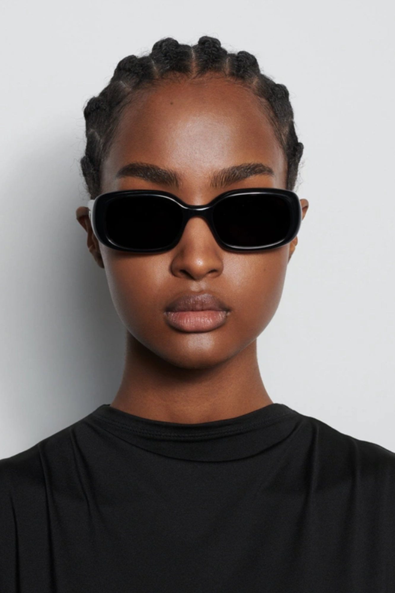 Person wearing black sunglasses and a black outfit against a white background