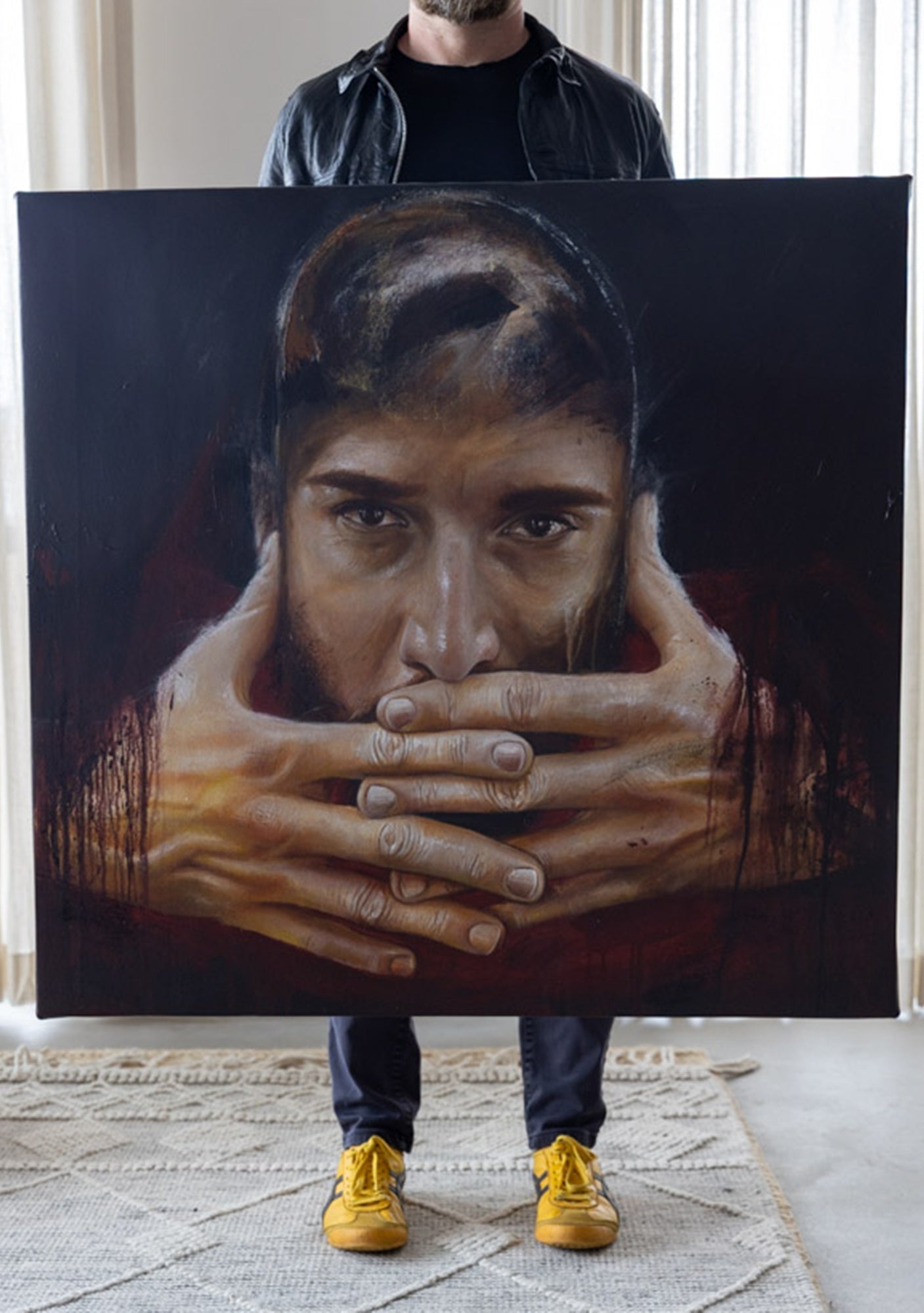 Person holding a large painting of a person with hands covering the face.